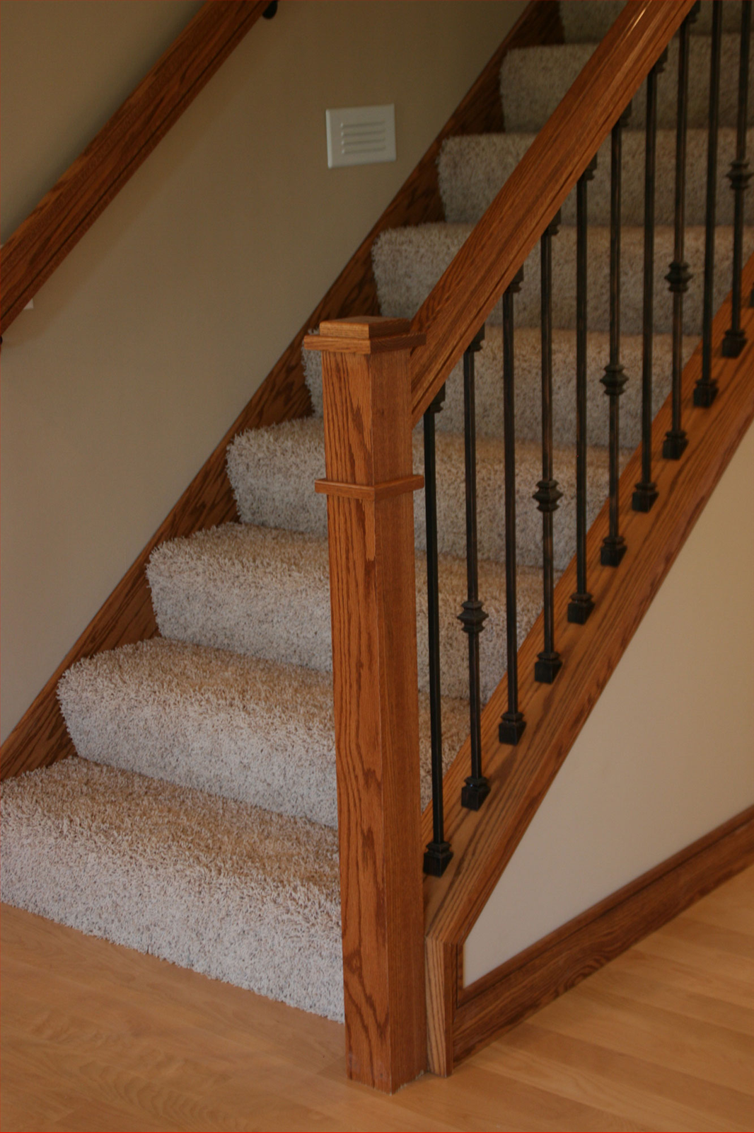 Wooden staircase with carpeted steps, dark metal spindles, and a wood banister.