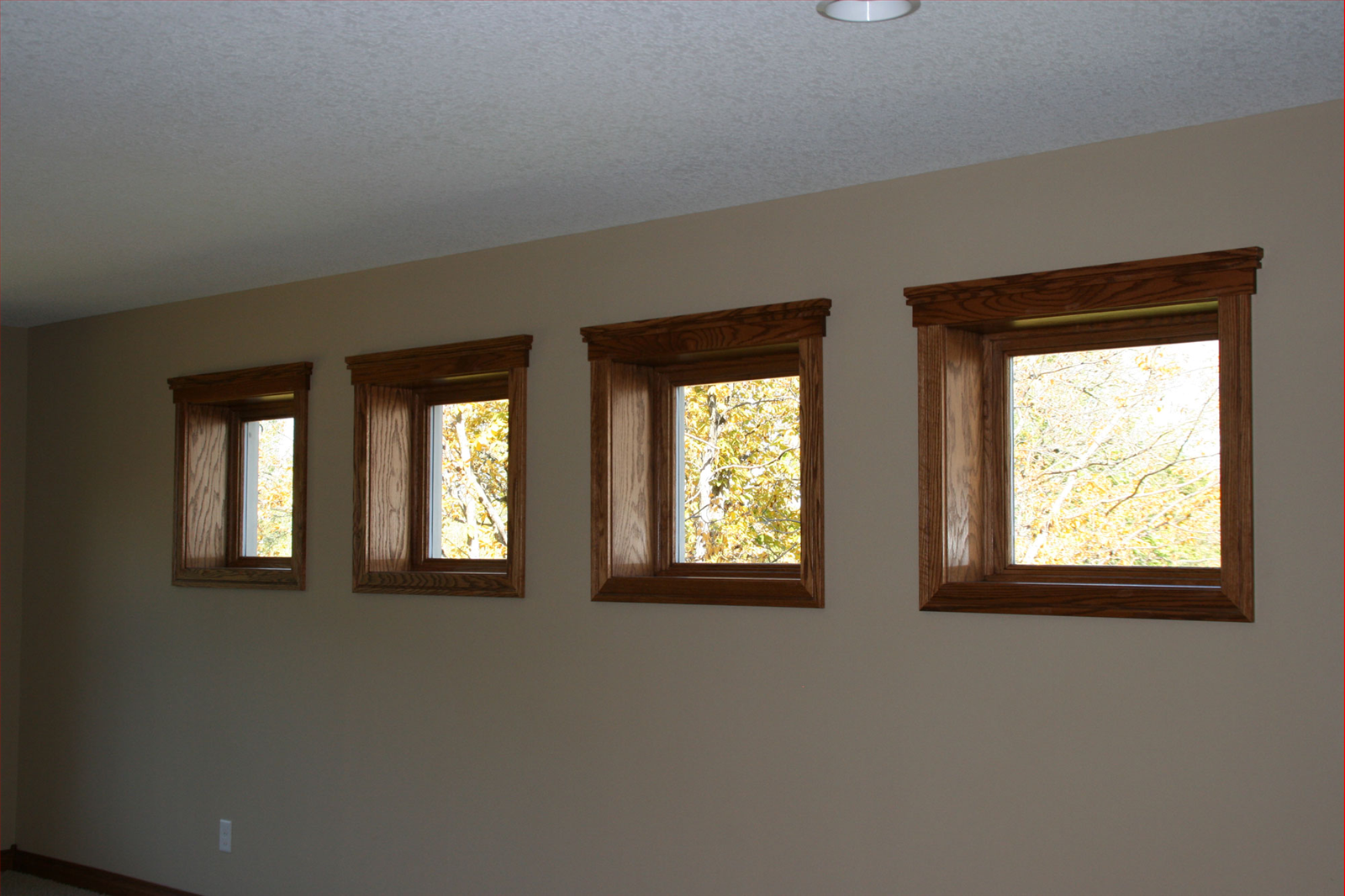 Four brown-framed windows in a row on a tan wall, with a view of trees outside.