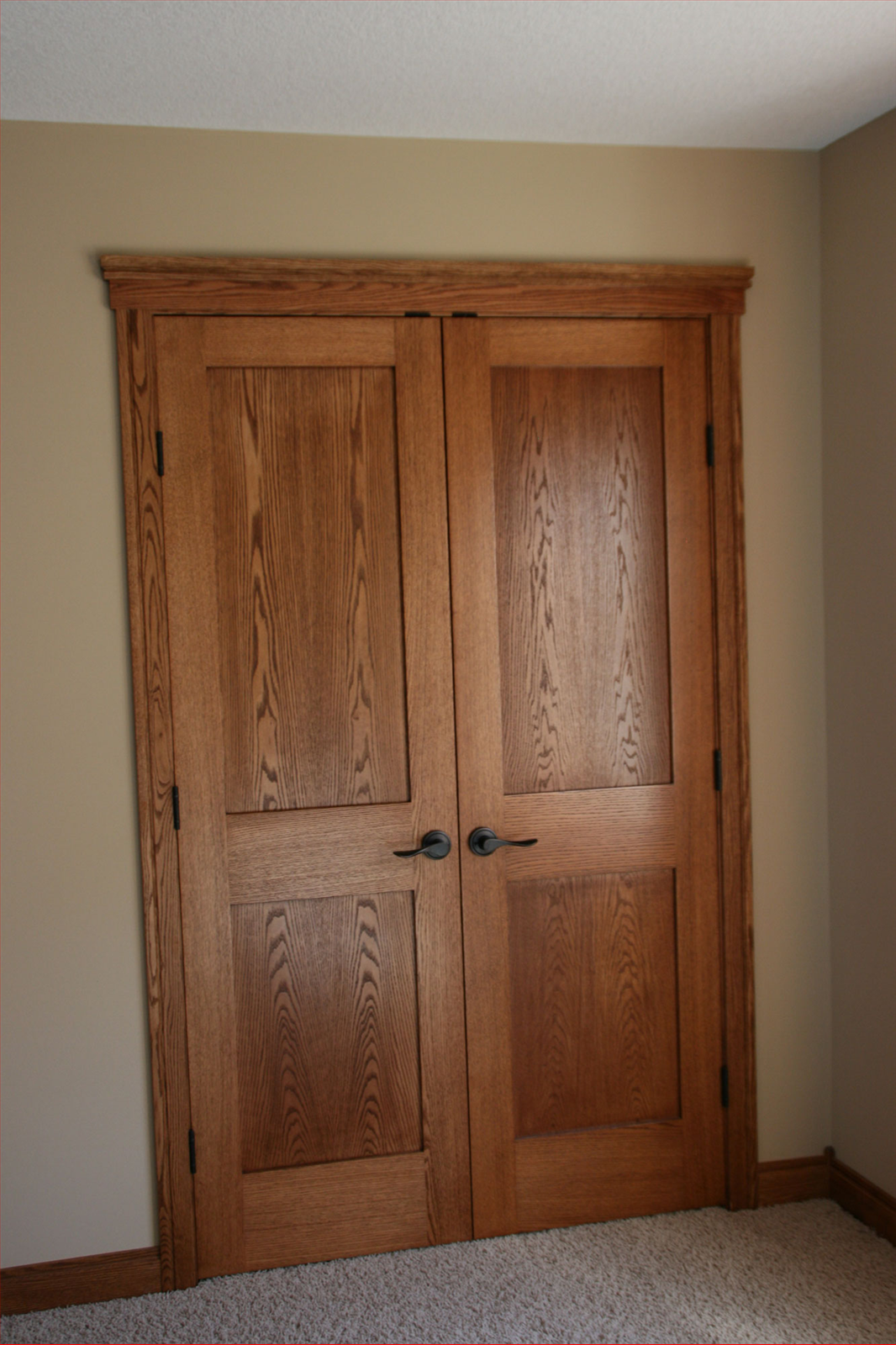 Wooden double doors with dark hardware and matching trim. Beige walls.