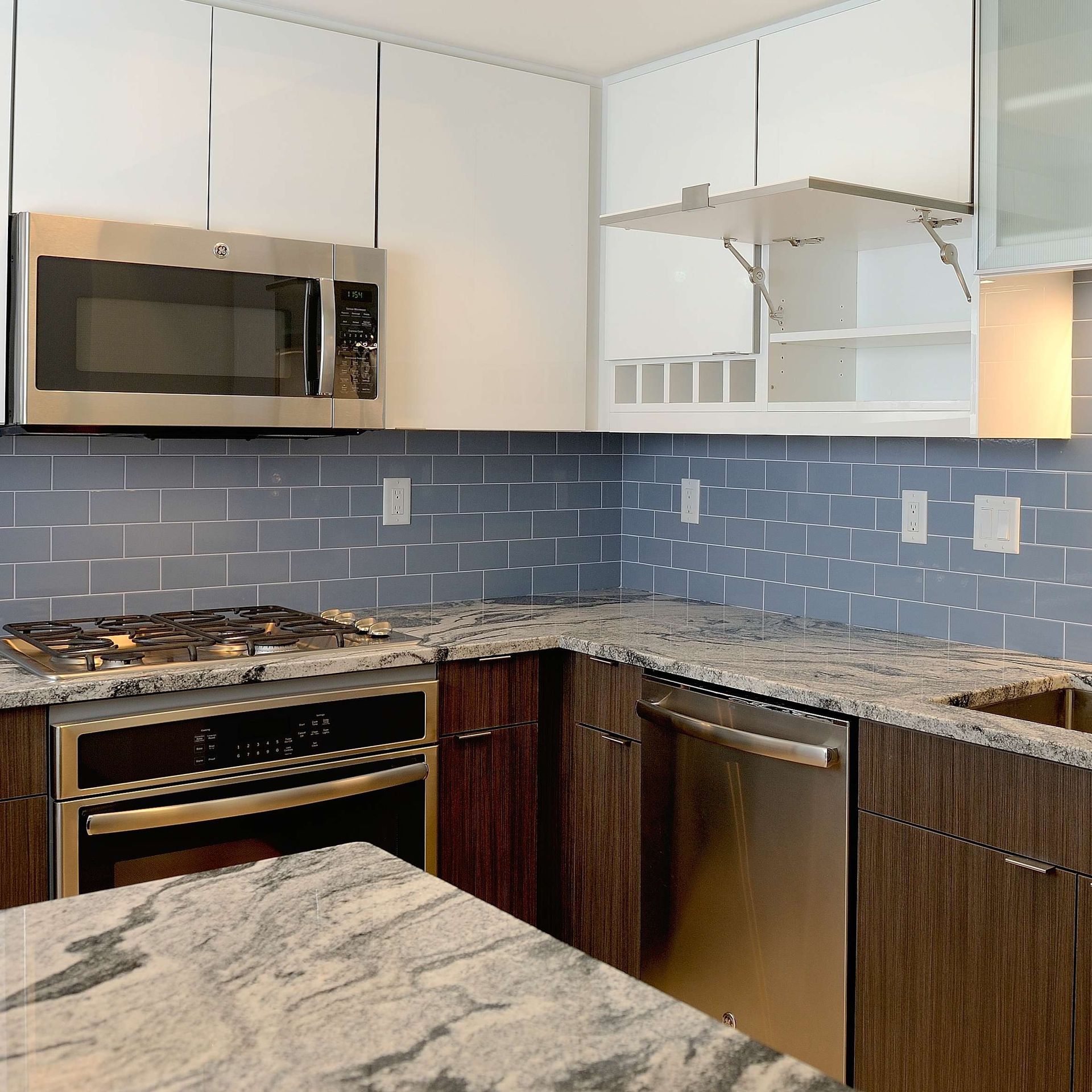 Modern kitchen with stainless steel appliances, blue tiled backsplash, and granite countertops.