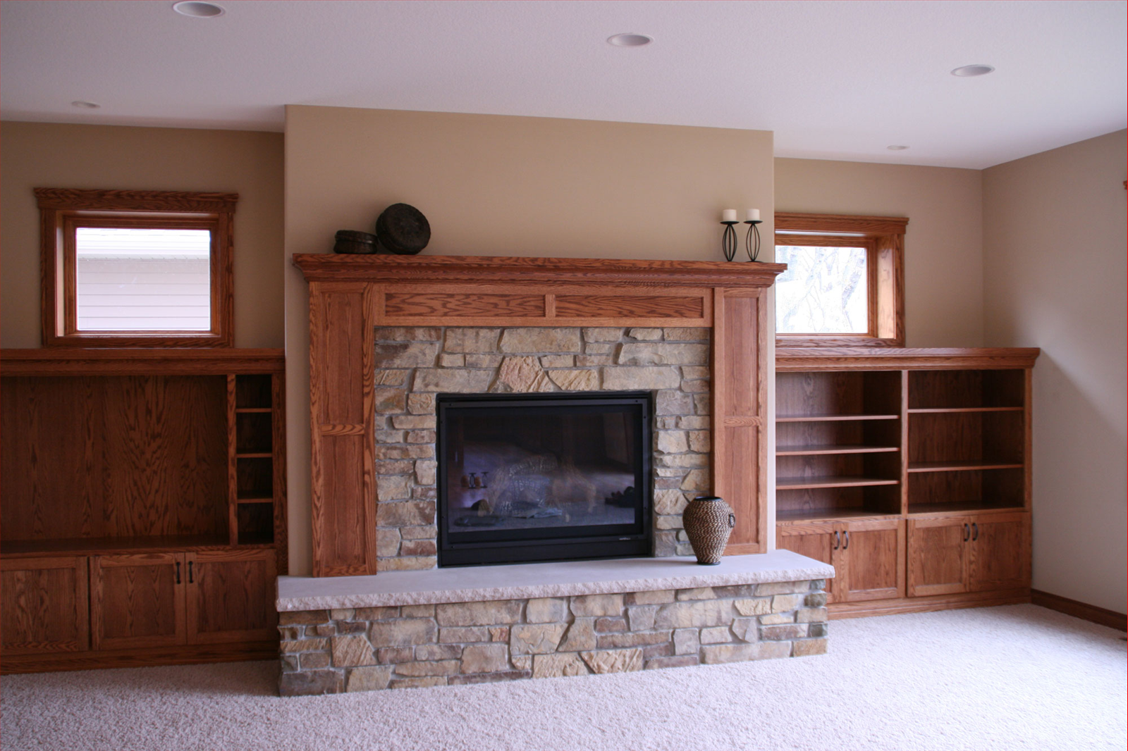 Fireplace with stone surround and wooden mantel flanked by built-in bookcases and windows.