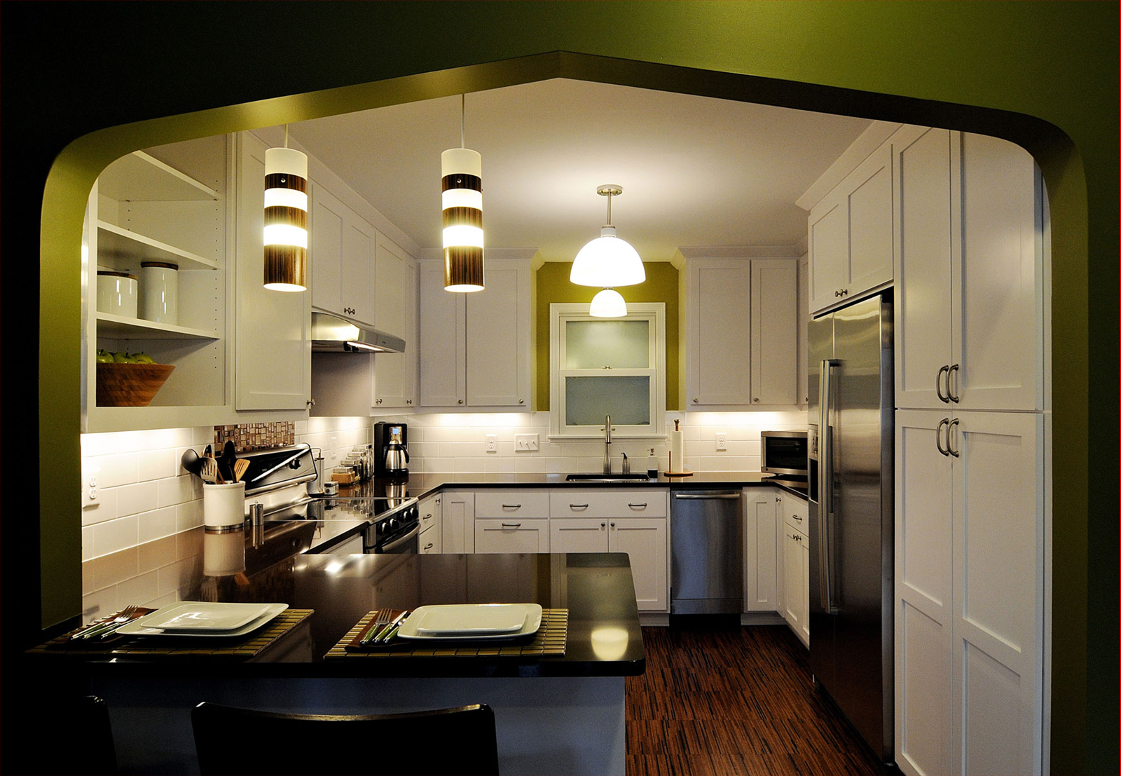 Modern kitchen with white cabinets, stainless steel appliances, dark countertops, and pendant lighting.