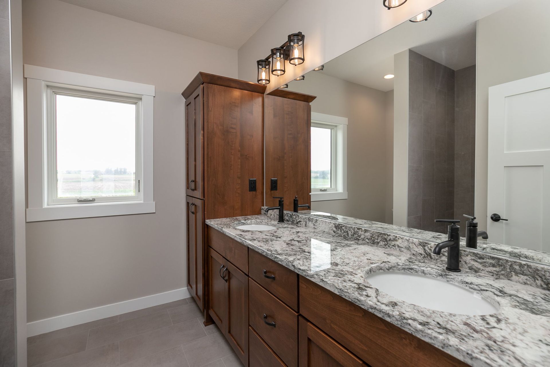 Bathroom with double vanity, granite countertop, brown cabinets, and large mirror.
