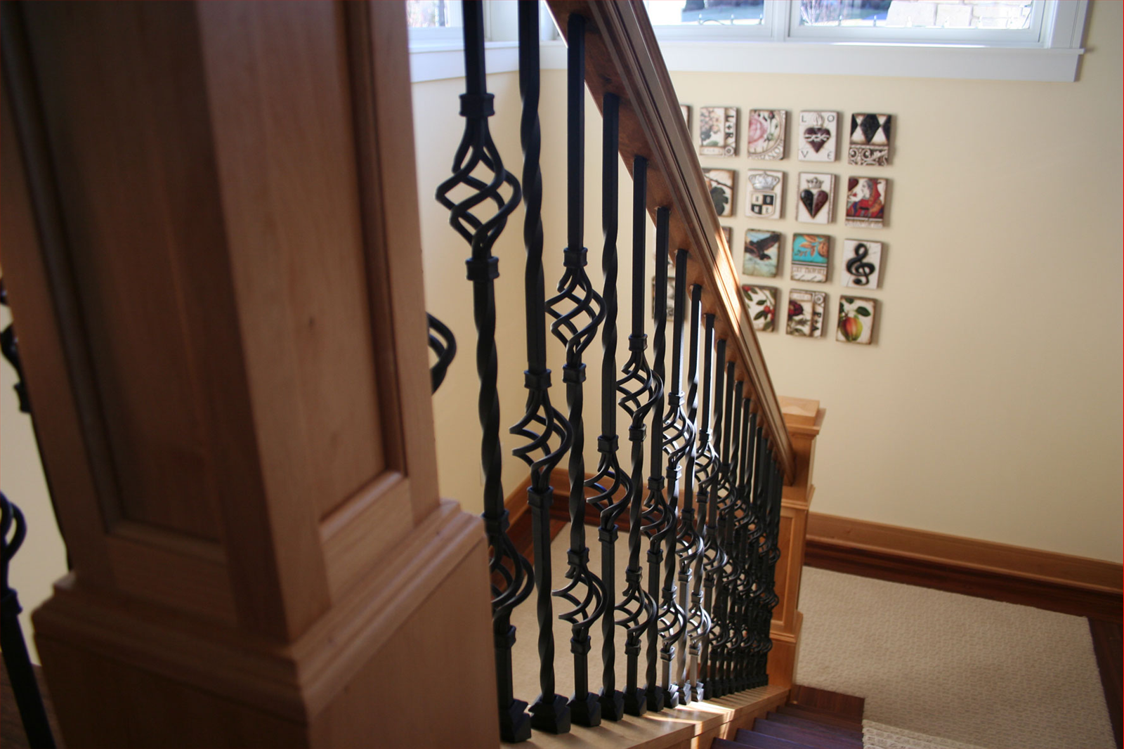 Wooden staircase with black metal balusters; art on the wall above.