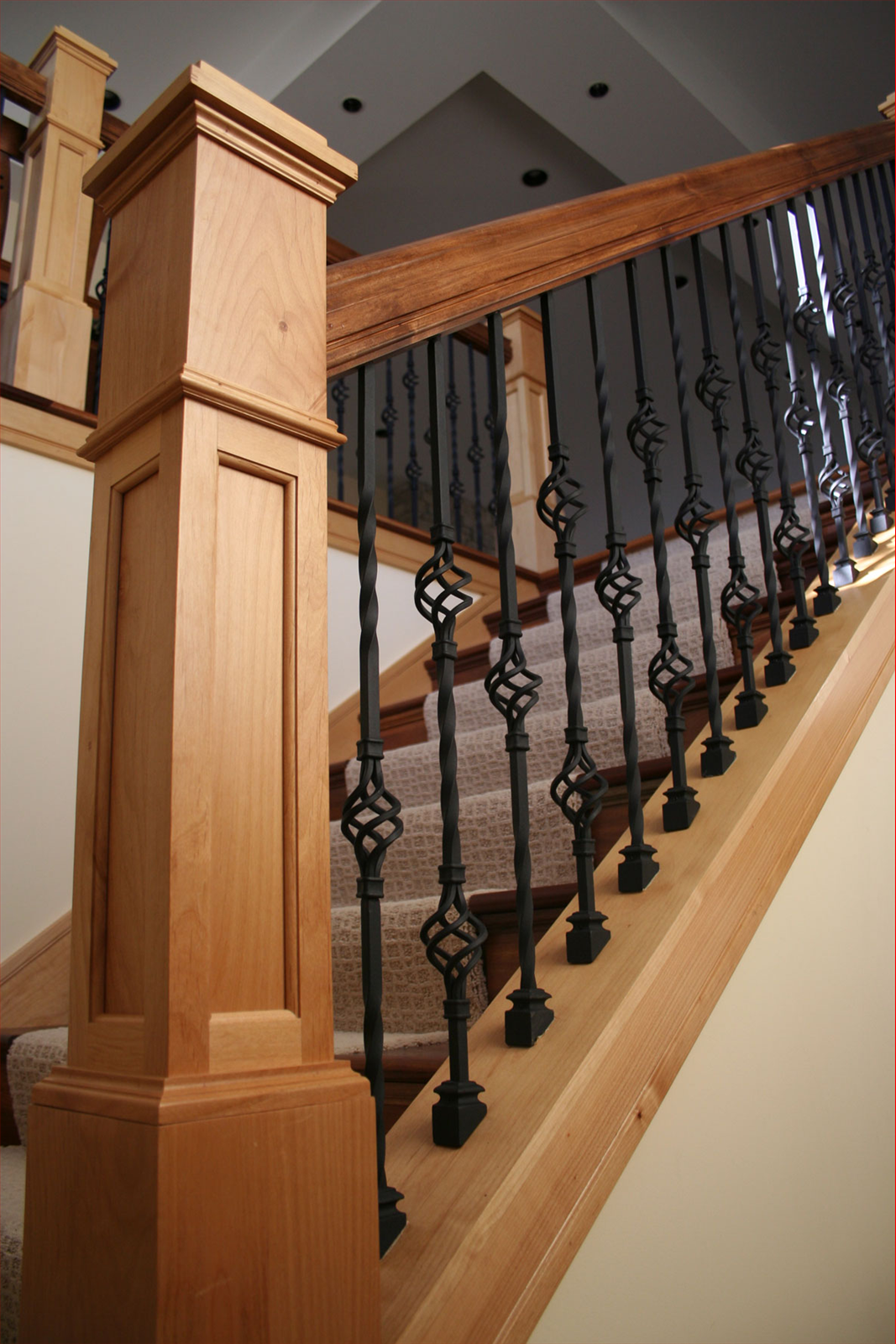 Wooden staircase with black metal balusters and a carpeted runner.