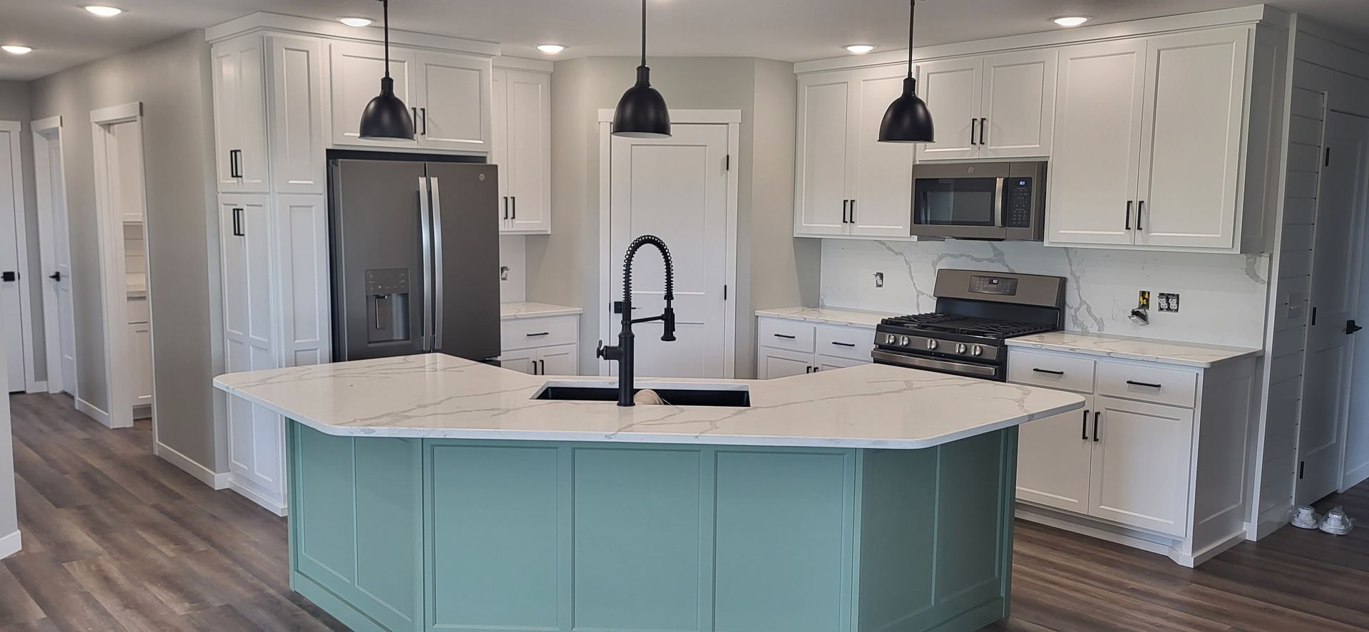 A kitchen with a blue island and white cabinets. Black light fixtures and appliances, with gray wood-look flooring.