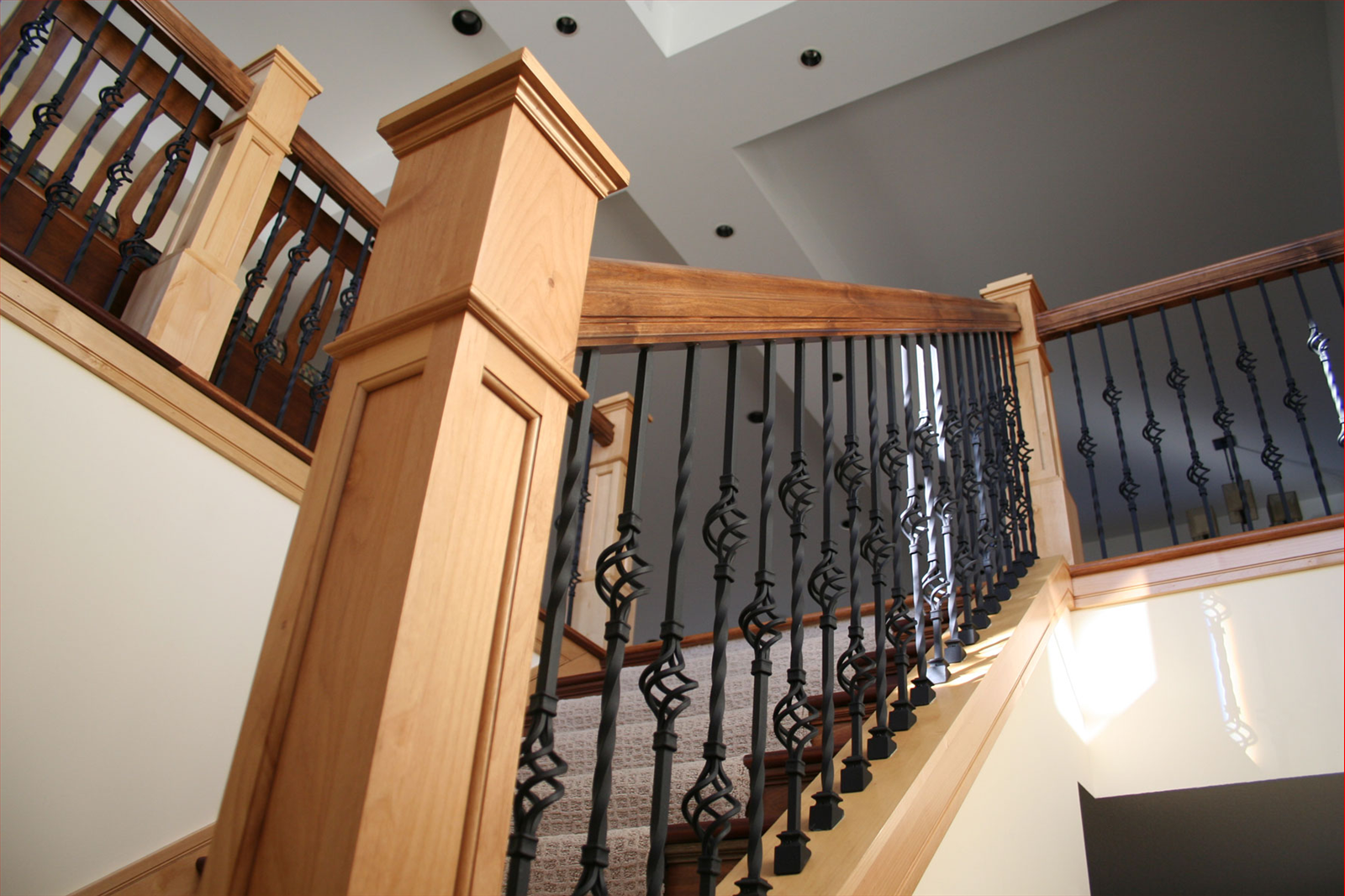 Wooden staircase with black wrought iron balusters and light-colored walls.