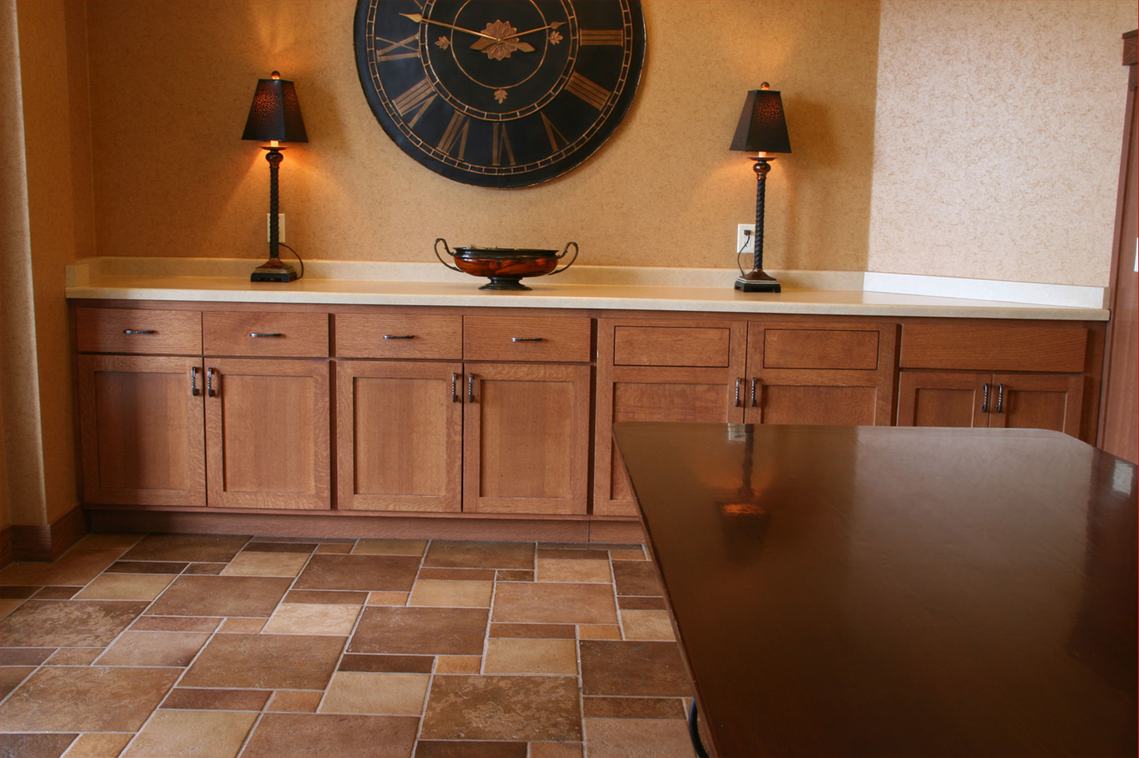 Wooden cabinets and tiled floor in a room, with a large clock and lamps on the wall.