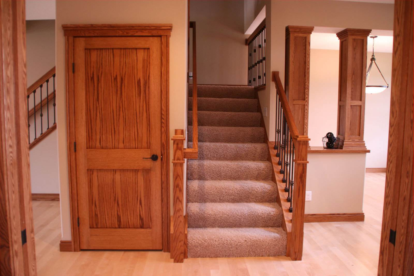 Wooden interior with door, staircase, and columns. Staircase has carpet, and railing. Door is closed.