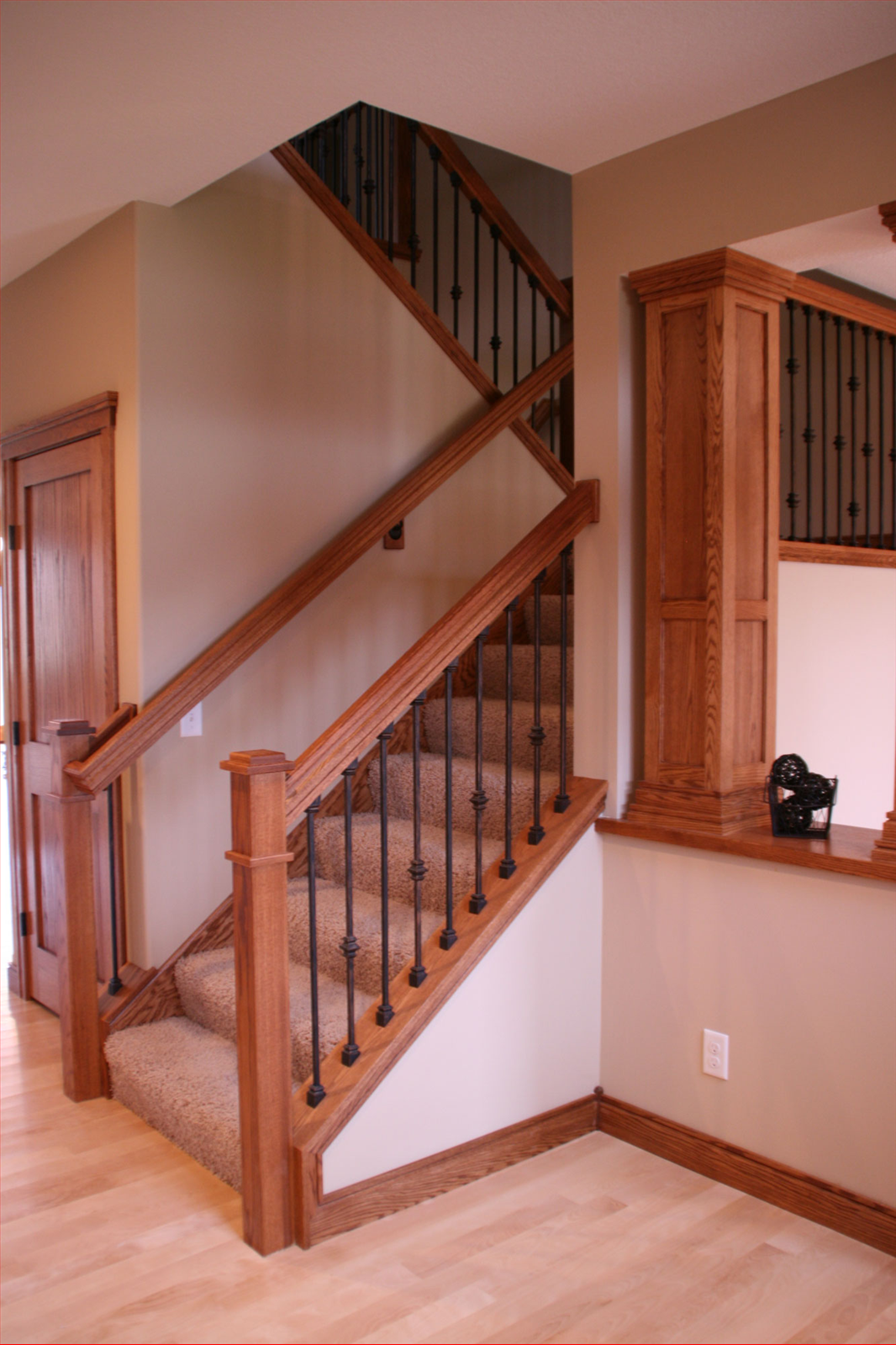 Wooden staircase with carpeted steps, dark metal balusters, and a light beige wall.