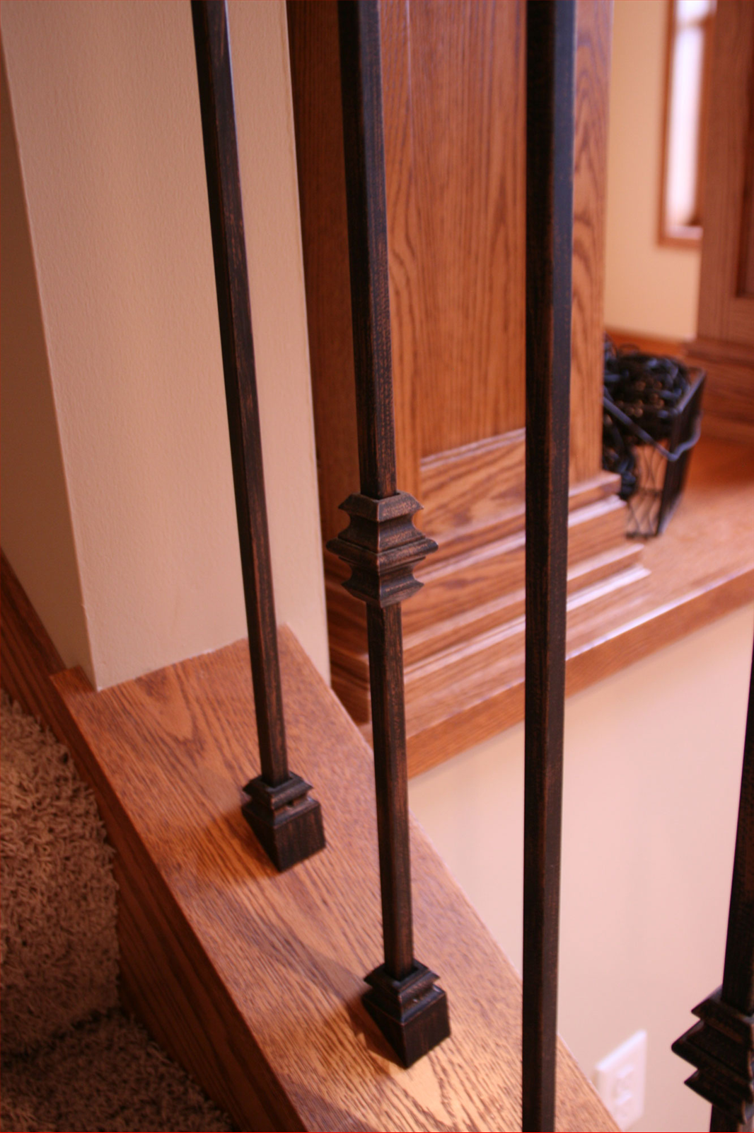 Black metal stair balusters on a wooden staircase with a beige wall in the background.
