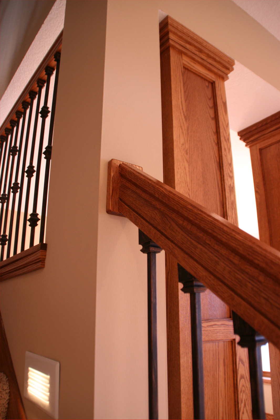 Wooden staircase with black metal balusters and detailed oak trim, next to a light-colored wall.