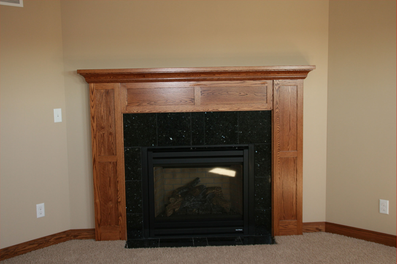 Fireplace with dark green tile surround and wooden mantel in a room with tan walls.