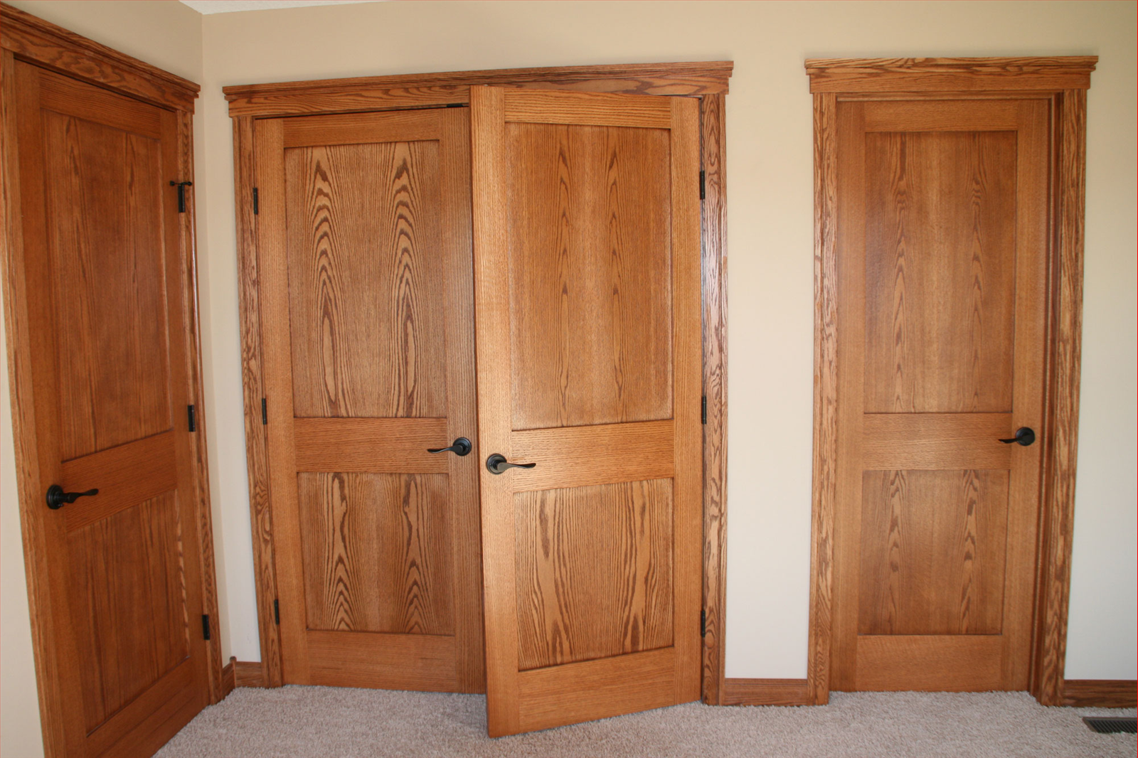 Three wooden doors with dark hardware, one open, in a room with light carpet and trim.