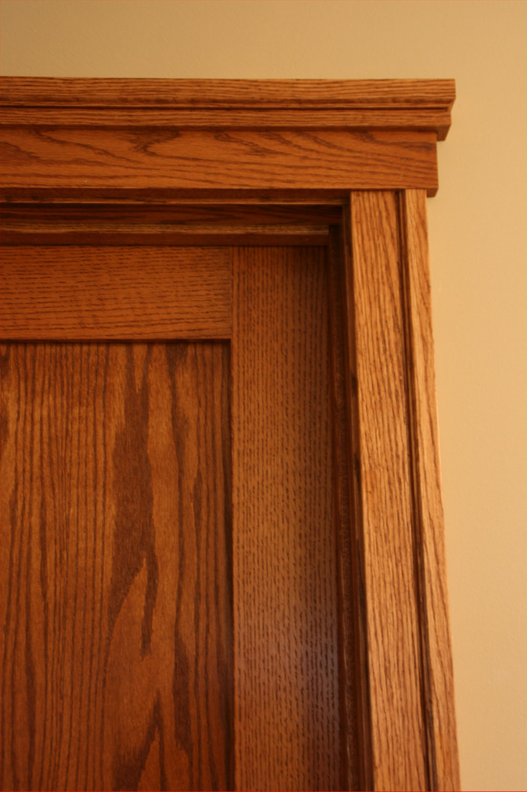 Close-up of a stained oak door and frame with detailed crown molding.