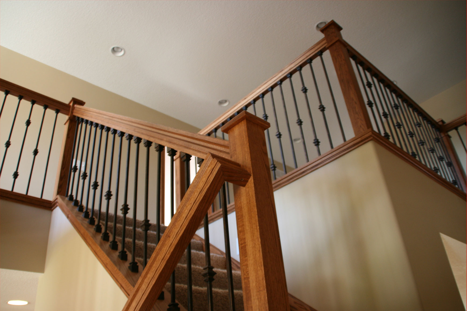 Wooden staircase with black metal balusters and brown carpet.