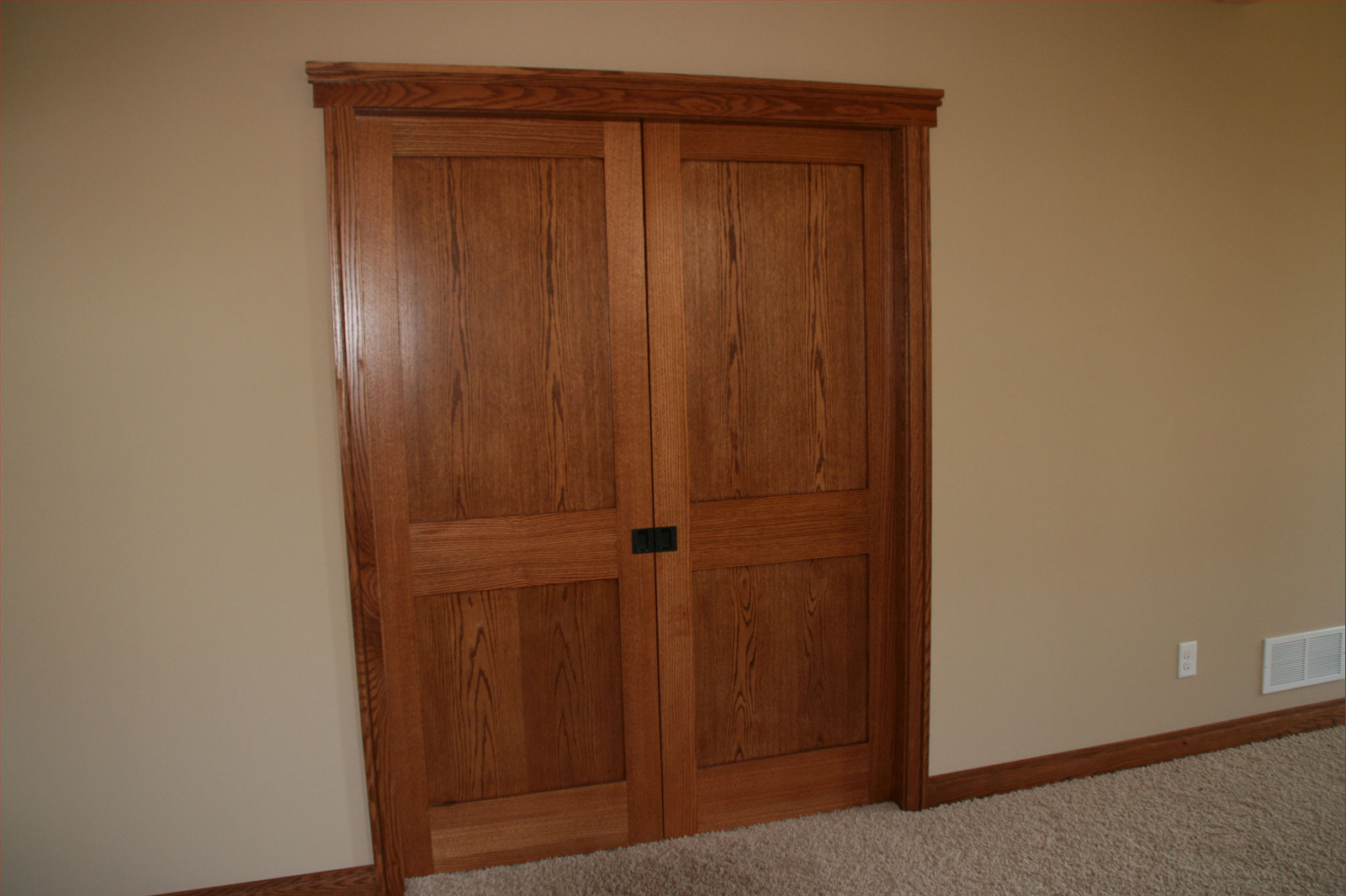 Double wooden doors with dark hardware, framed against tan walls and beige carpet.