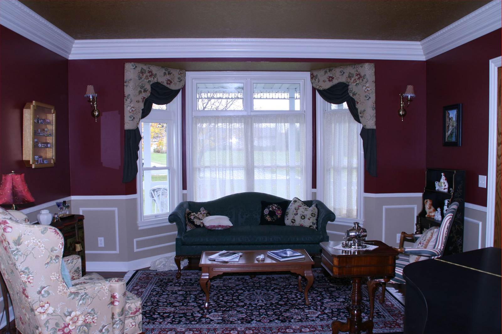 Living room with burgundy walls, white trim, and a green couch near a window with floral curtains.