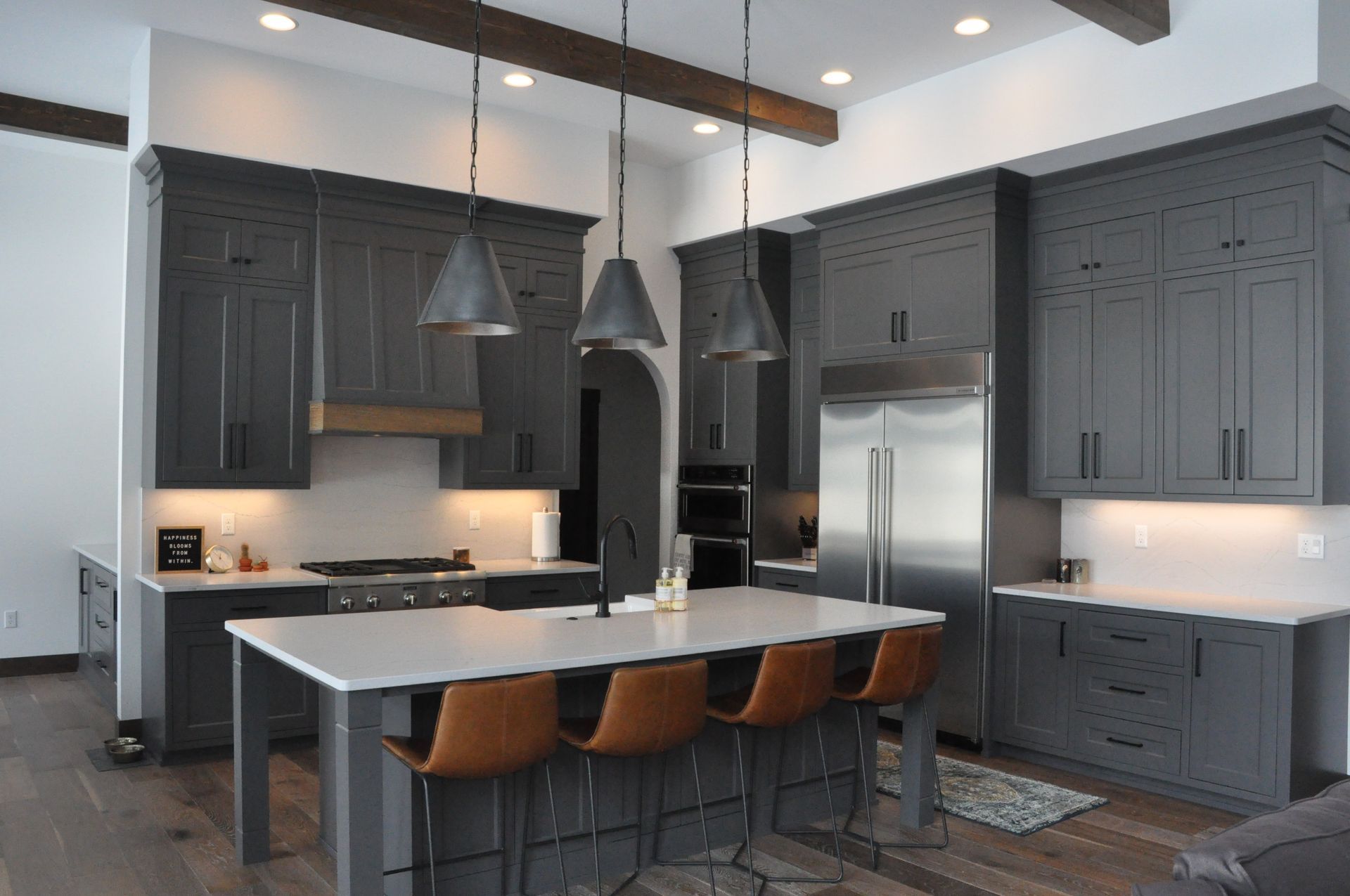 Gray kitchen with island, stainless steel appliances, pendant lights, brown bar stools.