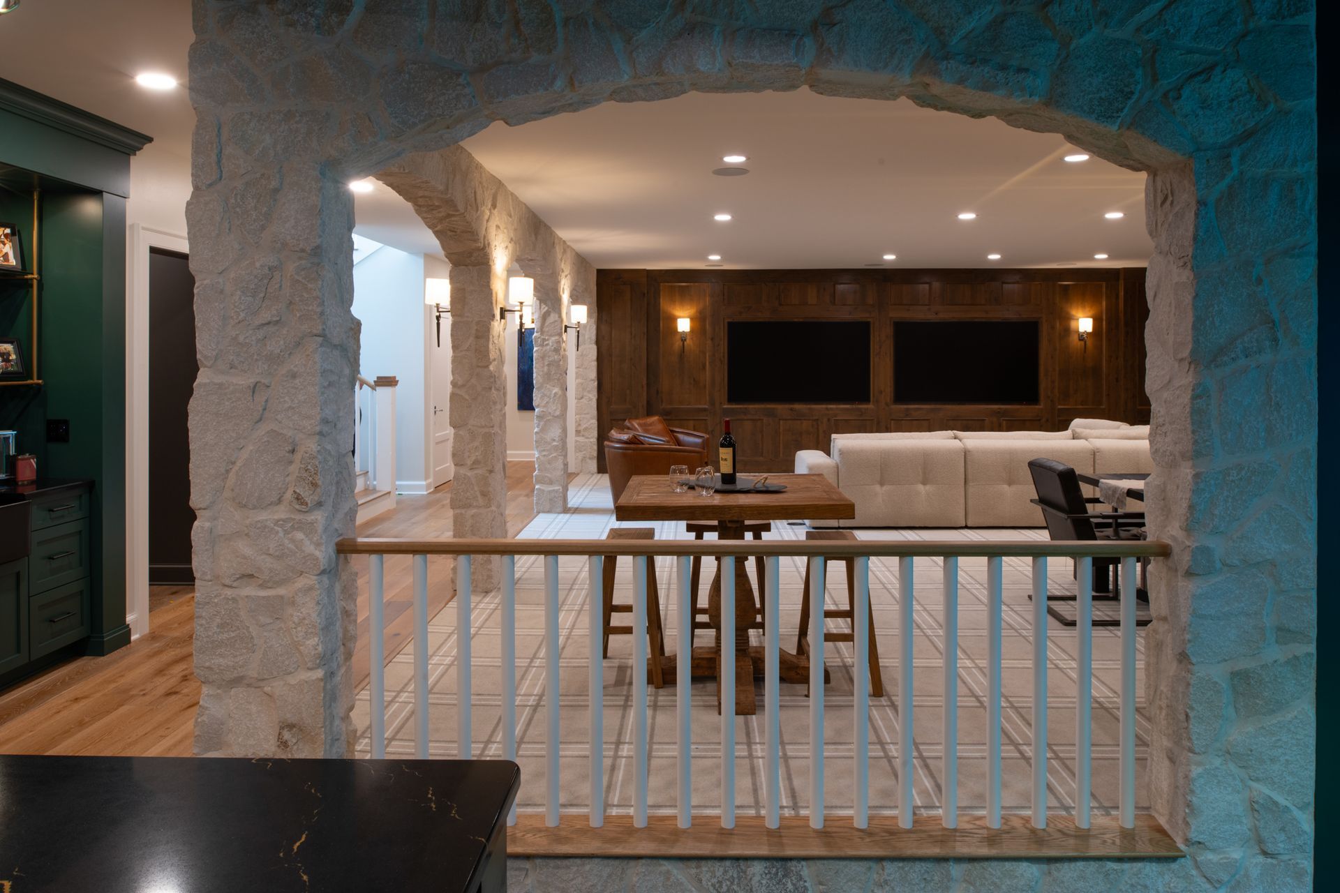 Stone archway overlooks a basement entertainment area with a bar, seating, and two large screens.