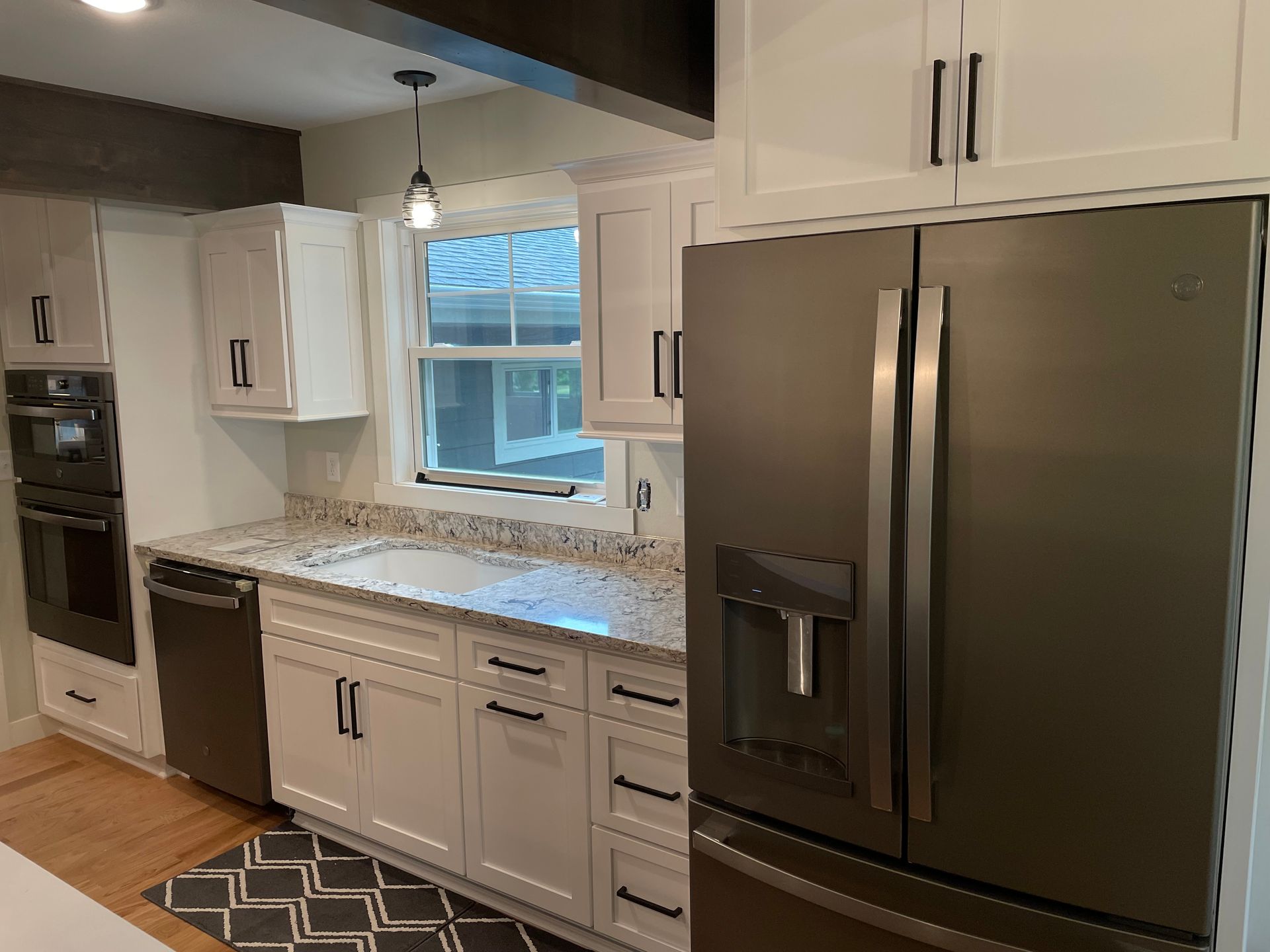 Modern kitchen with white cabinets, stainless steel refrigerator, granite countertops, and black hardware.