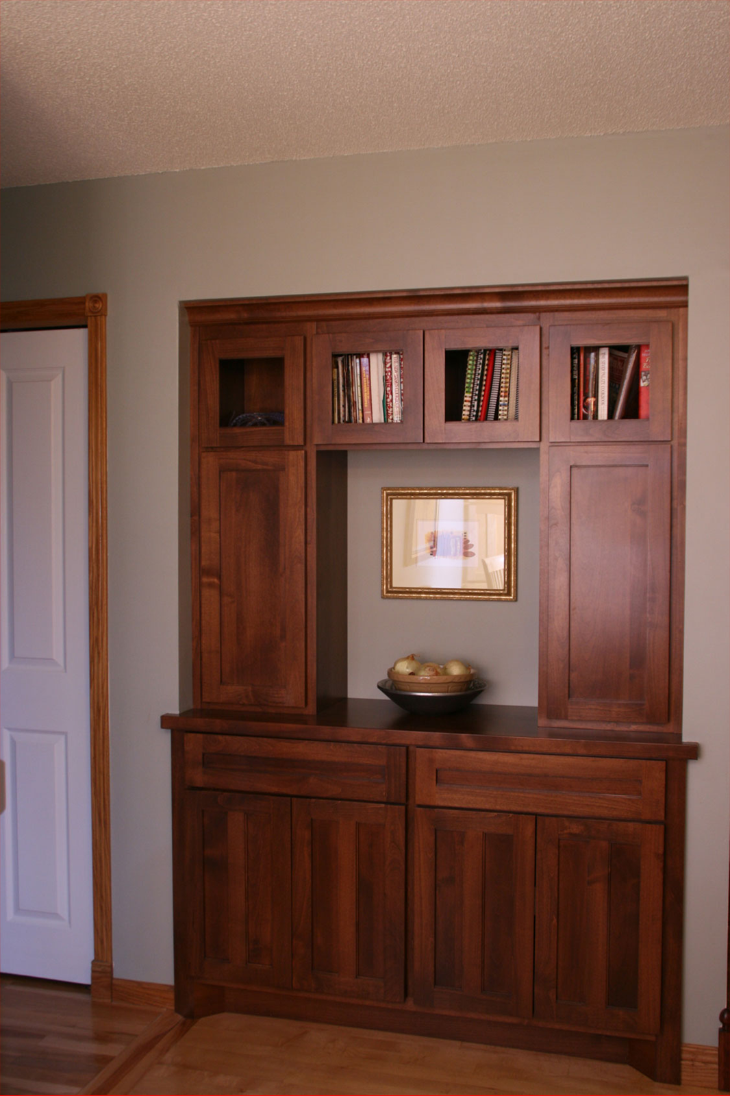 Built-in wooden cabinet in a wall niche, with closed doors, glass-fronted shelves, and a display area.