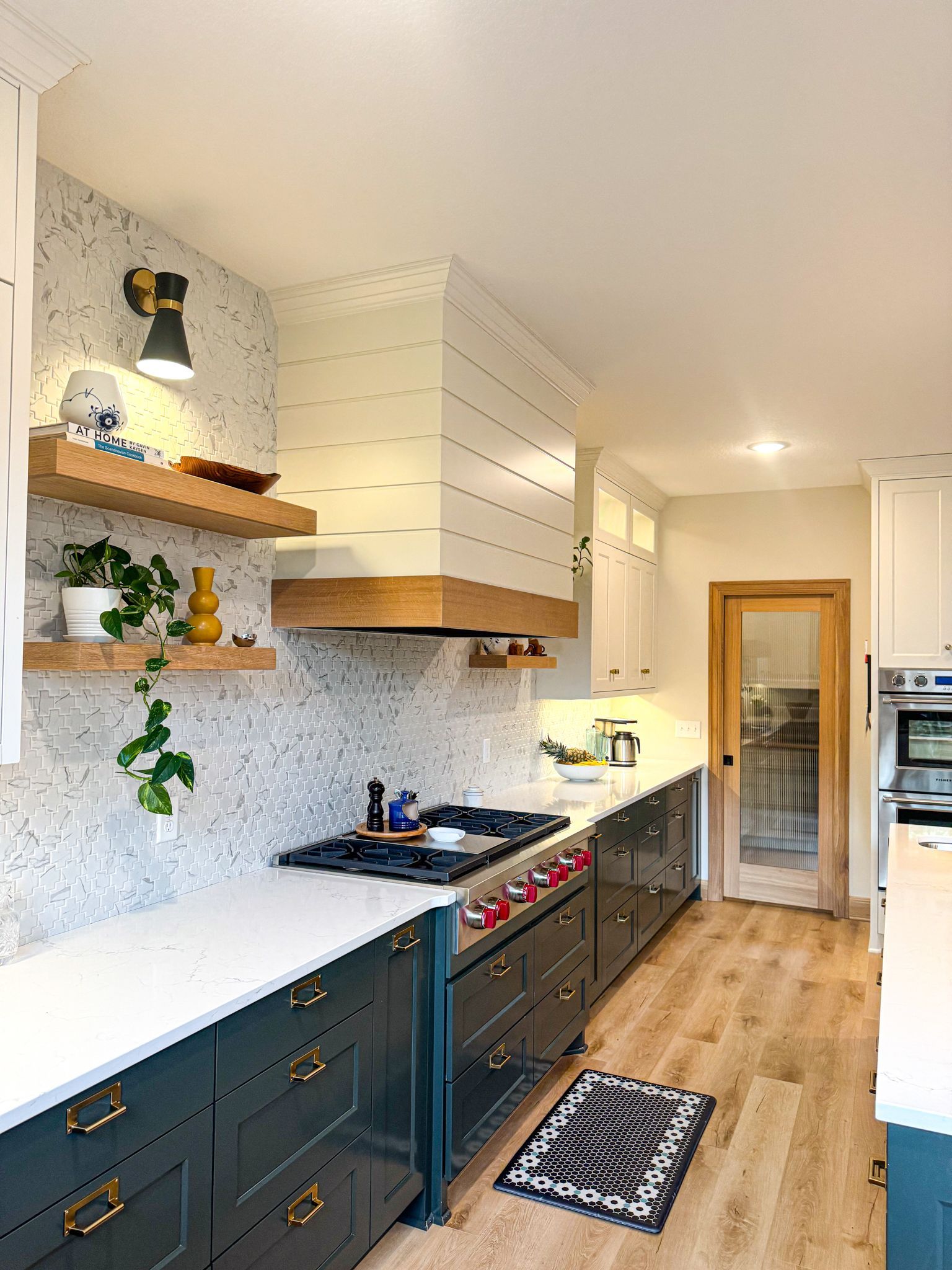 Modern kitchen with dark teal cabinets, white countertops, wood accents, and a patterned backsplash.