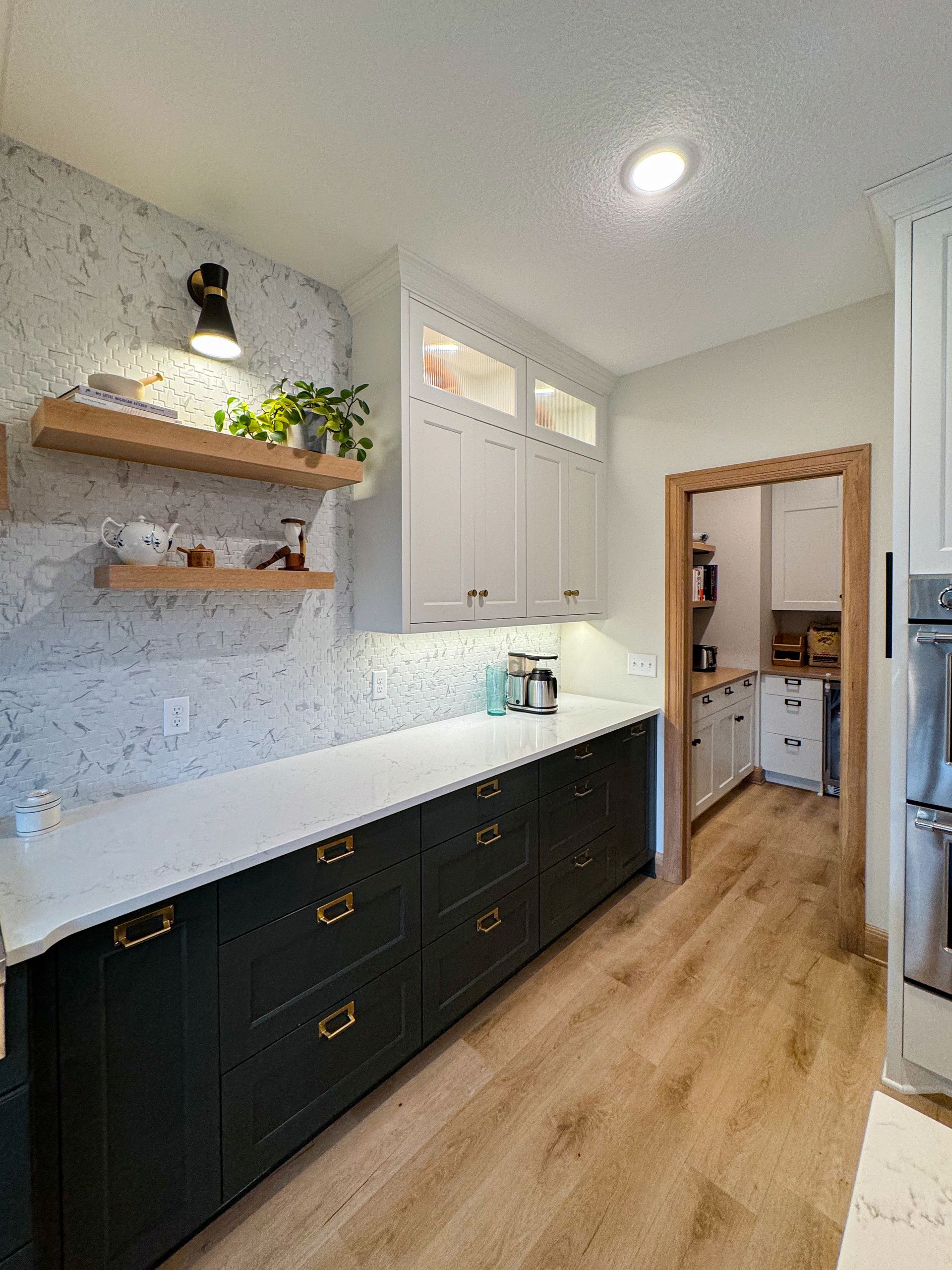 Kitchen with black and white cabinets, white countertops, wood shelves, and a pantry.