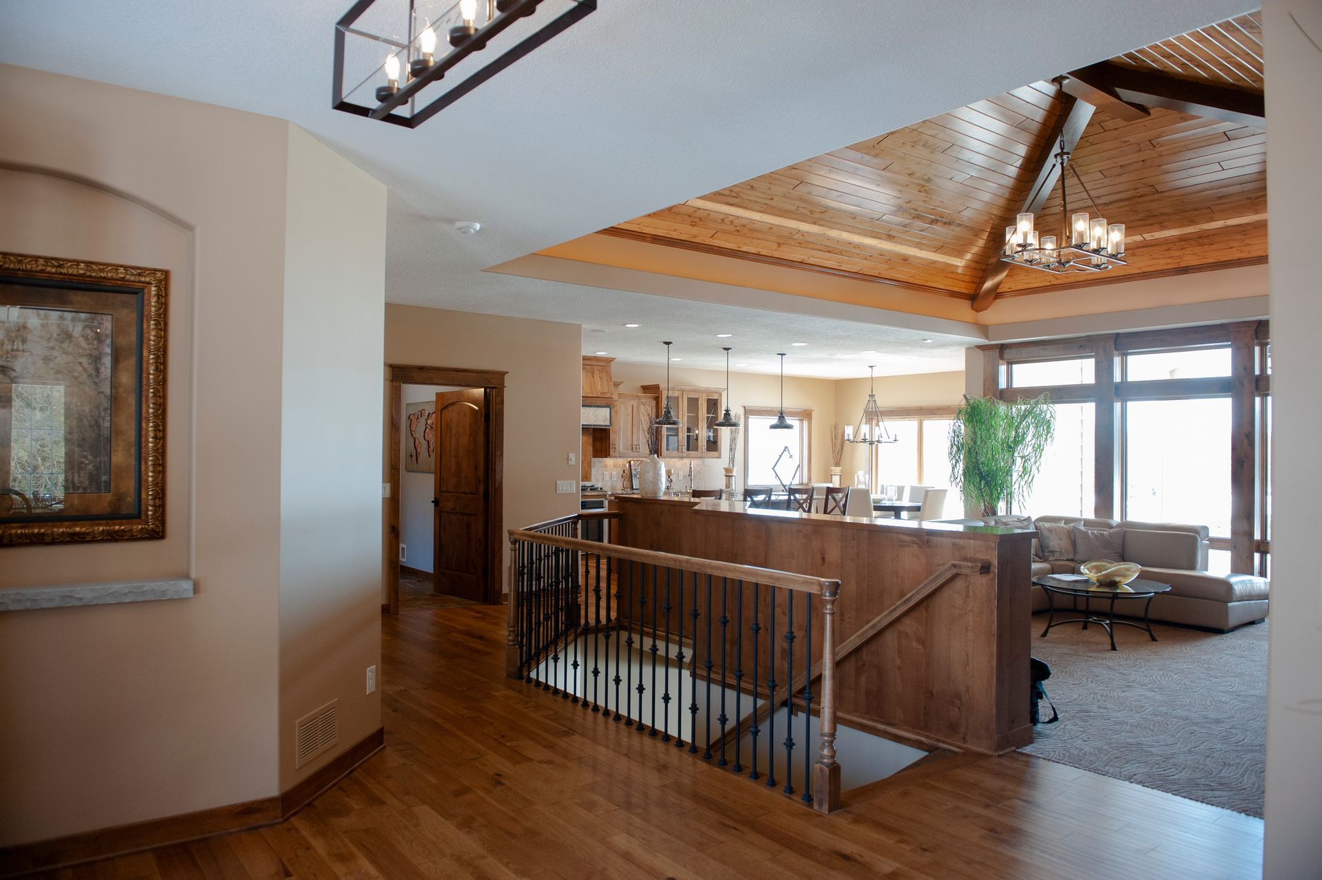 Interior view of a home with a wooden staircase, hardwood floors, and a living area with large windows.