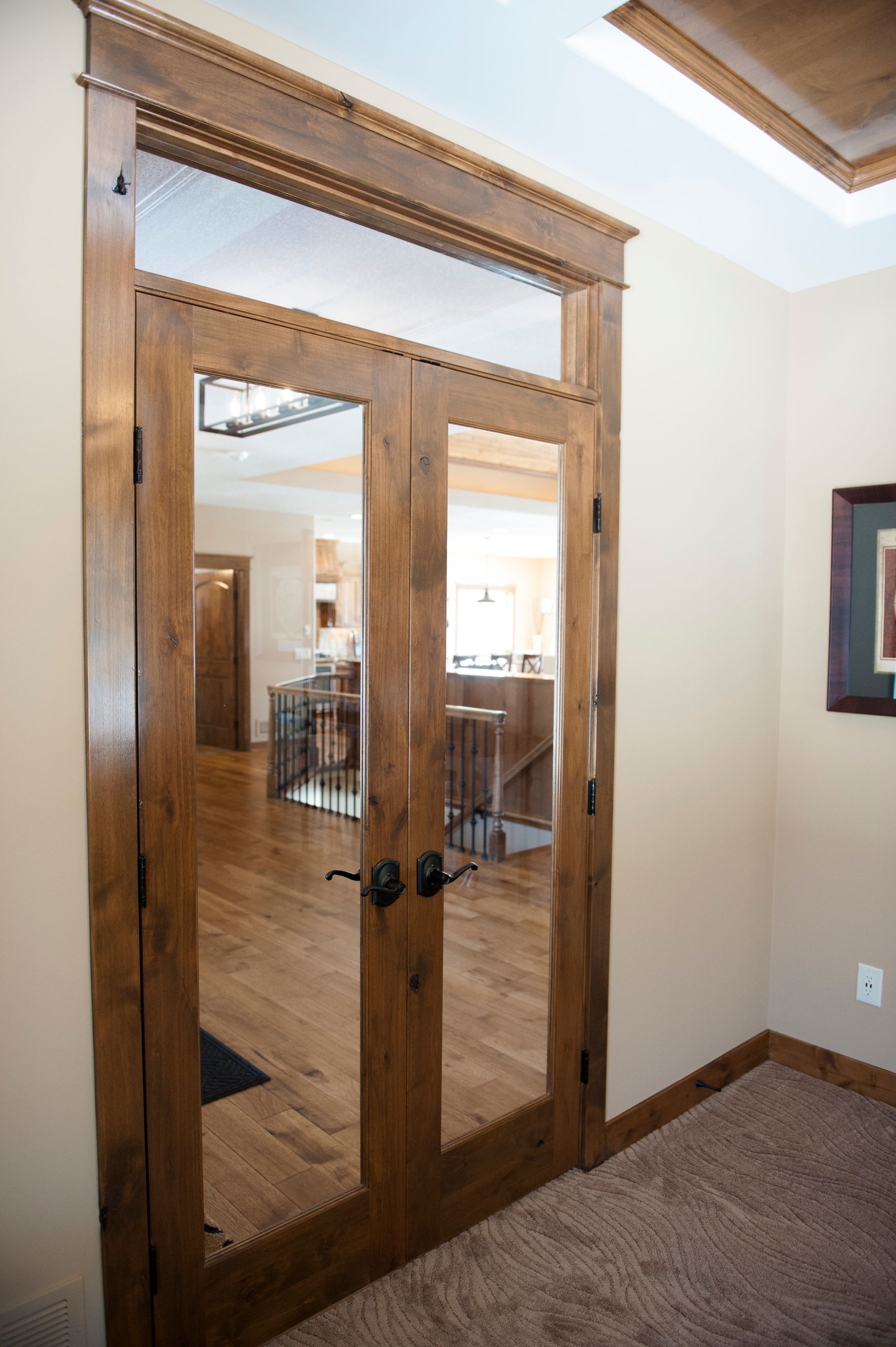 Wooden double doors with glass panels and textured glass transom, opening to a well-lit interior.