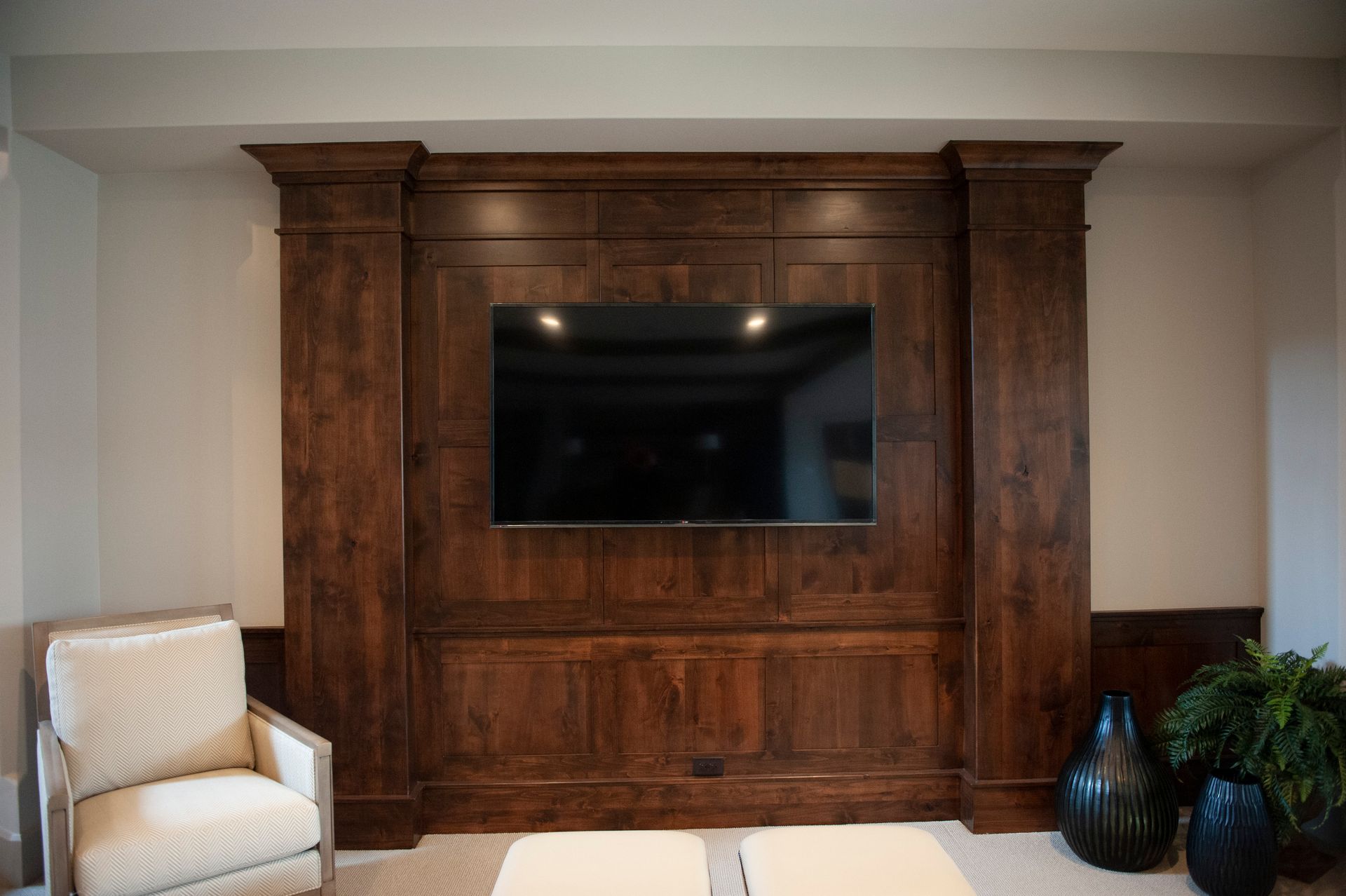 A dark wood media center with a mounted TV, flanked by columns. An armchair and decorative vases are in the room.