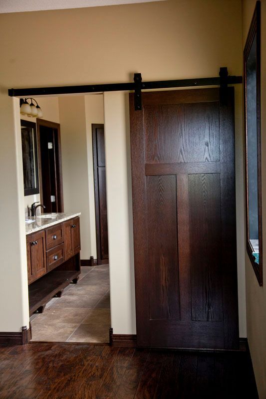 Dark wooden sliding barn door partially open to a bathroom with a vanity.