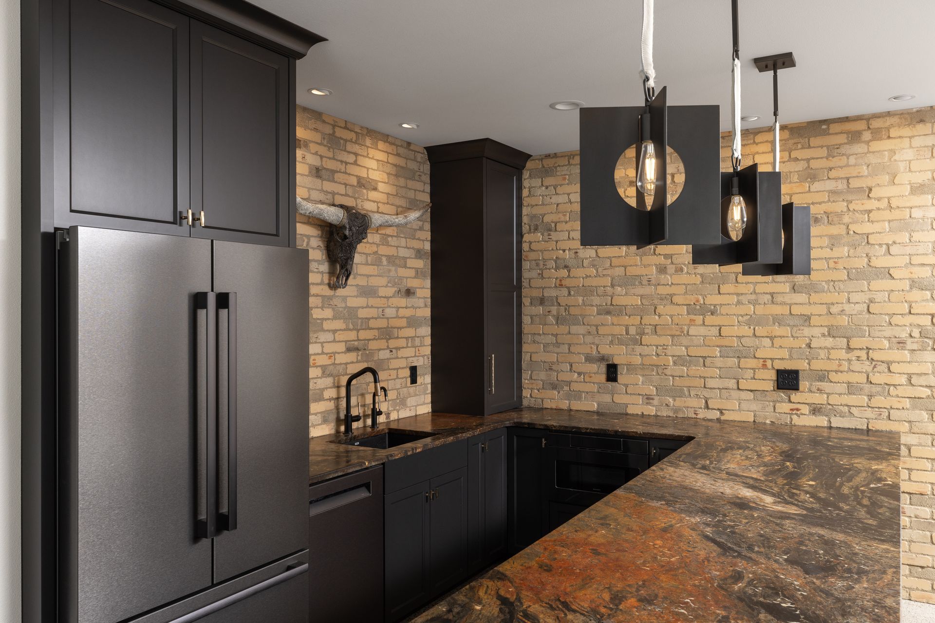 Black kitchen with brick wall, granite countertop, modern pendant lights, and black refrigerator.