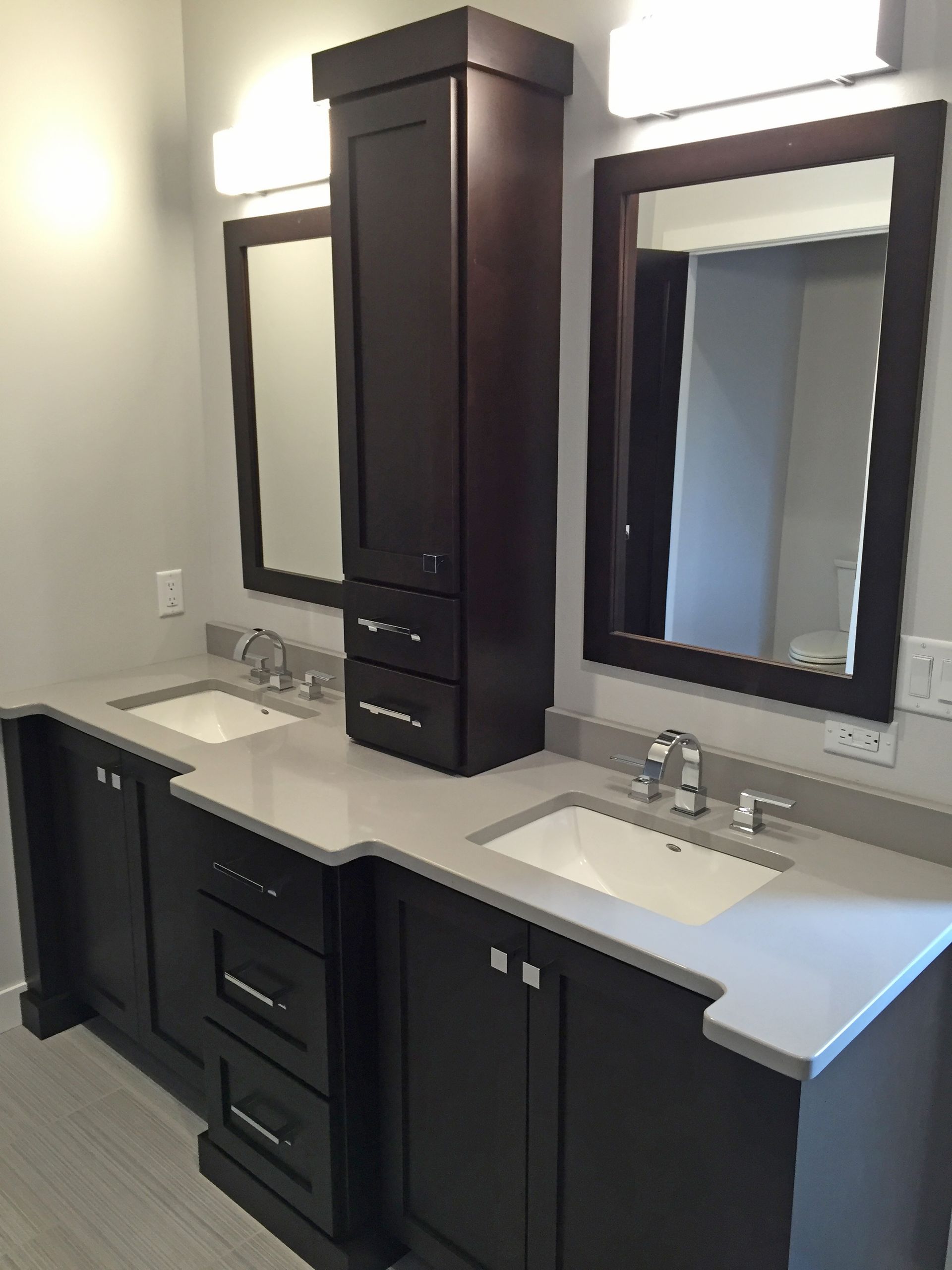 Bathroom vanity with dark cabinets, light countertops, mirrors, and a tall storage cabinet.