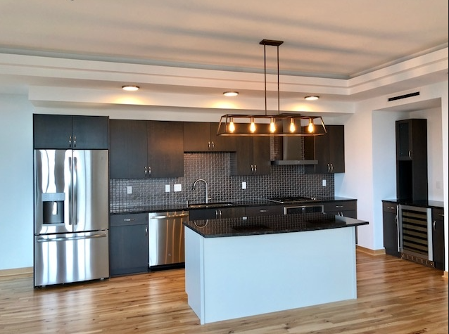 Modern kitchen with dark cabinetry, stainless steel appliances, and a black island.