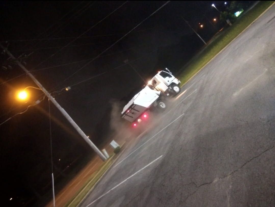 A garbage truck is parked in a parking lot at night