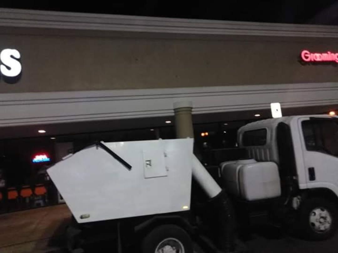 A dumpster truck is parked in front of a building that says grooming