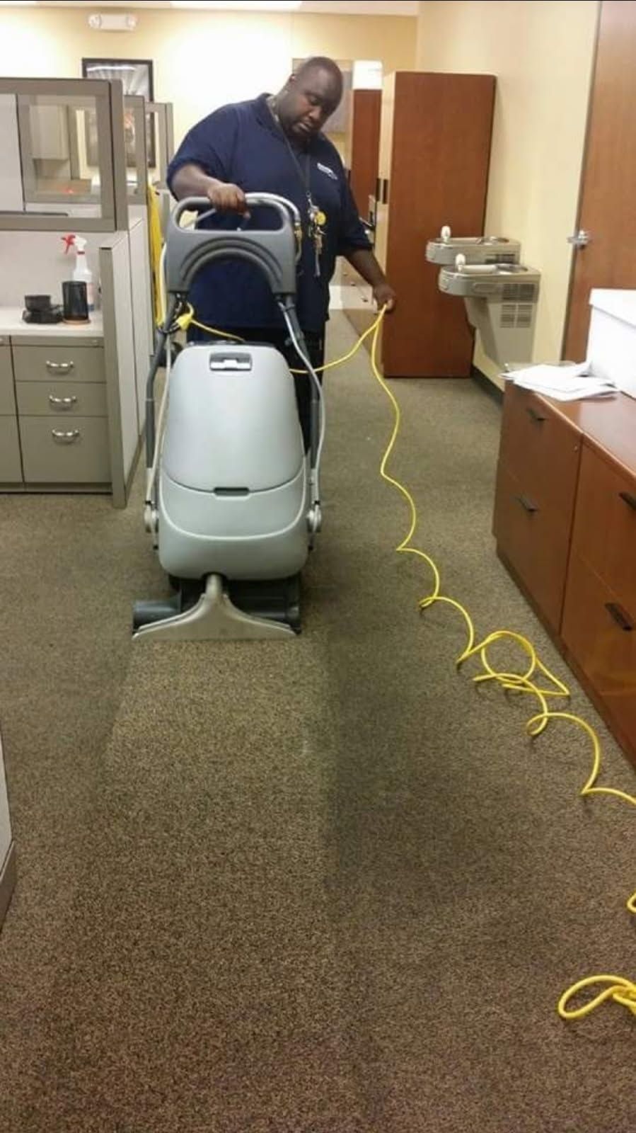 A man is using a vacuum cleaner to clean a carpet in an office.