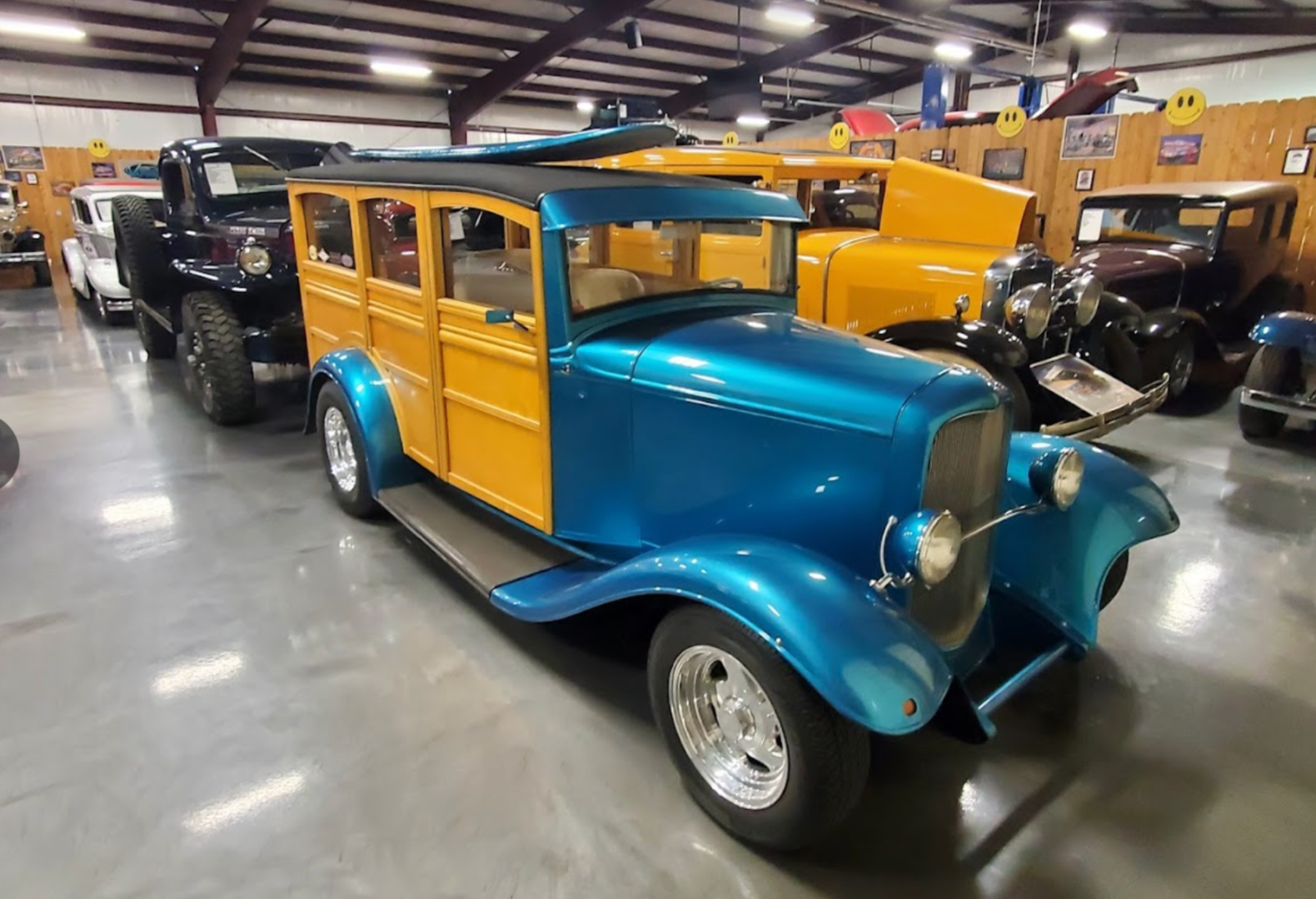 Blue and wood-paneled vintage car with a surfboard on top, in a car museum.