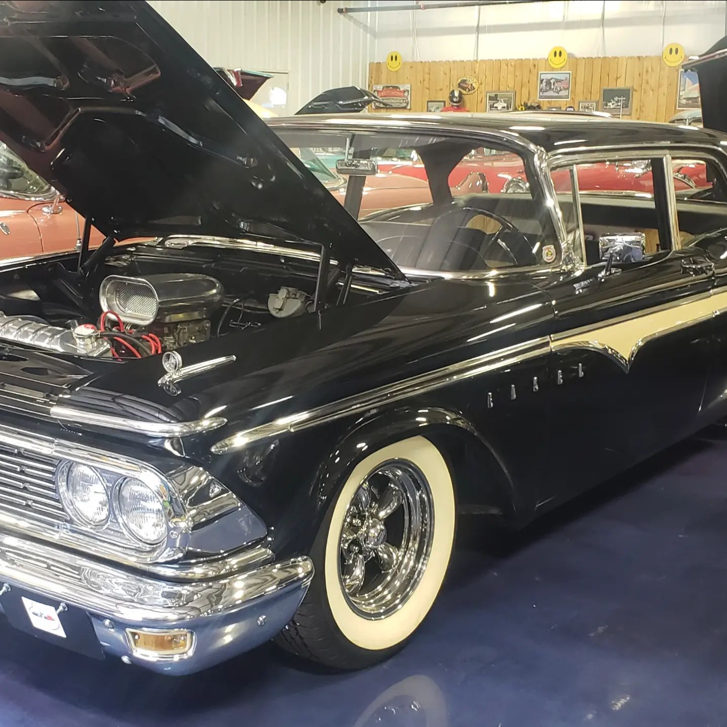 Black and cream classic car with hood open in a showroom. Chrome accents and whitewall tires.