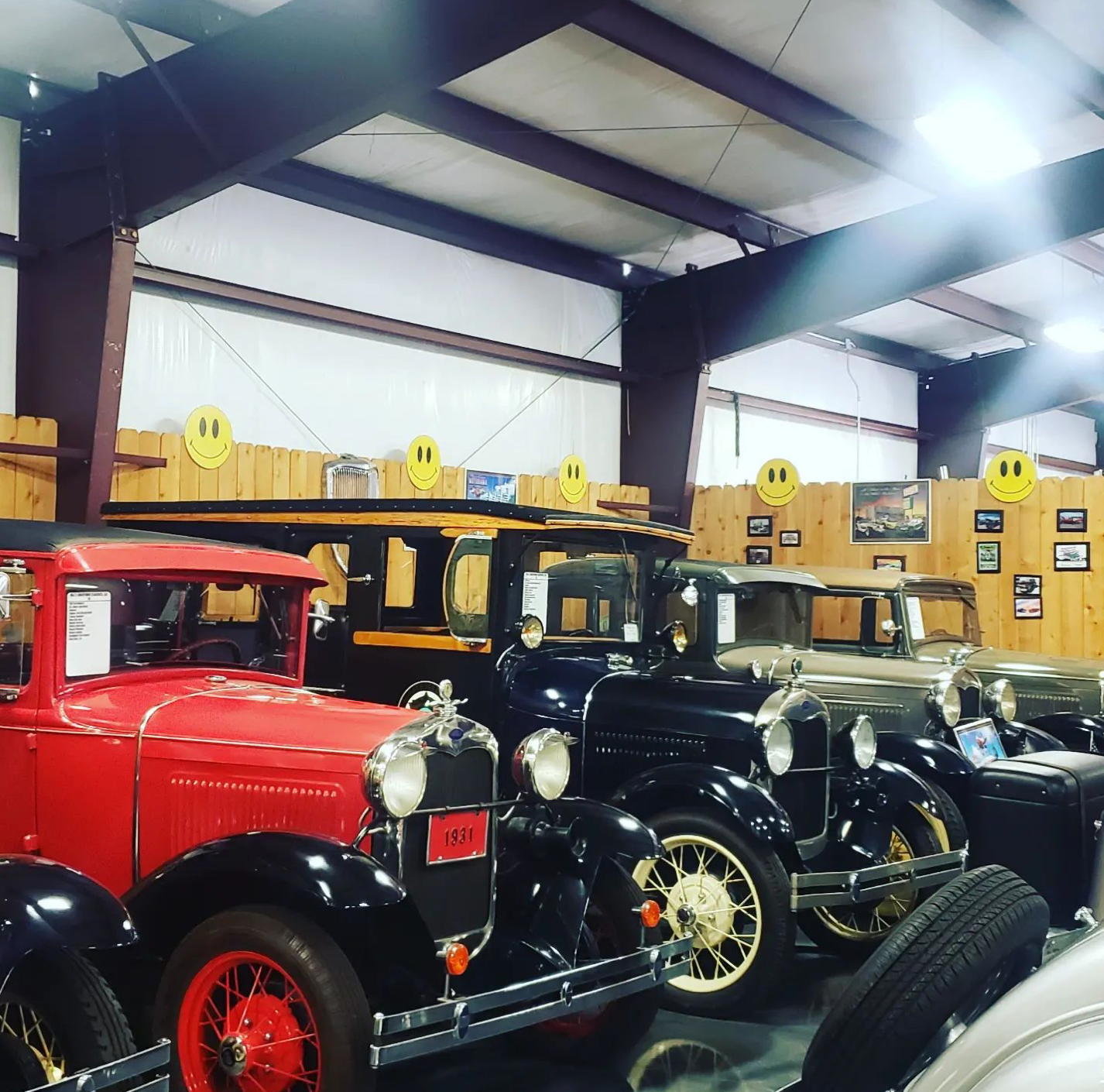 Classic cars on display in a large indoor setting with red, black, and tan vehicles.