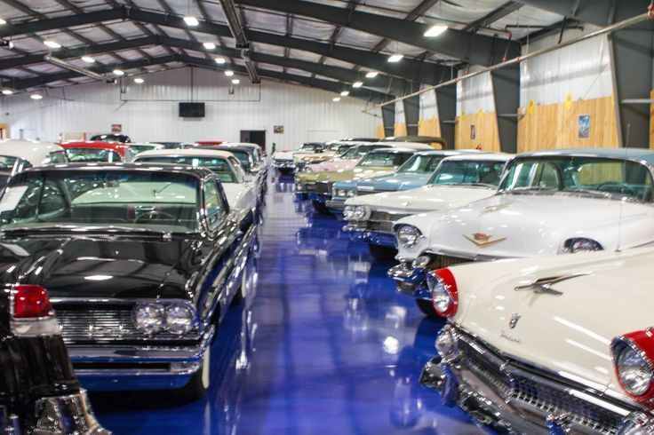 Rows of classic cars parked in a large, blue-floored garage.