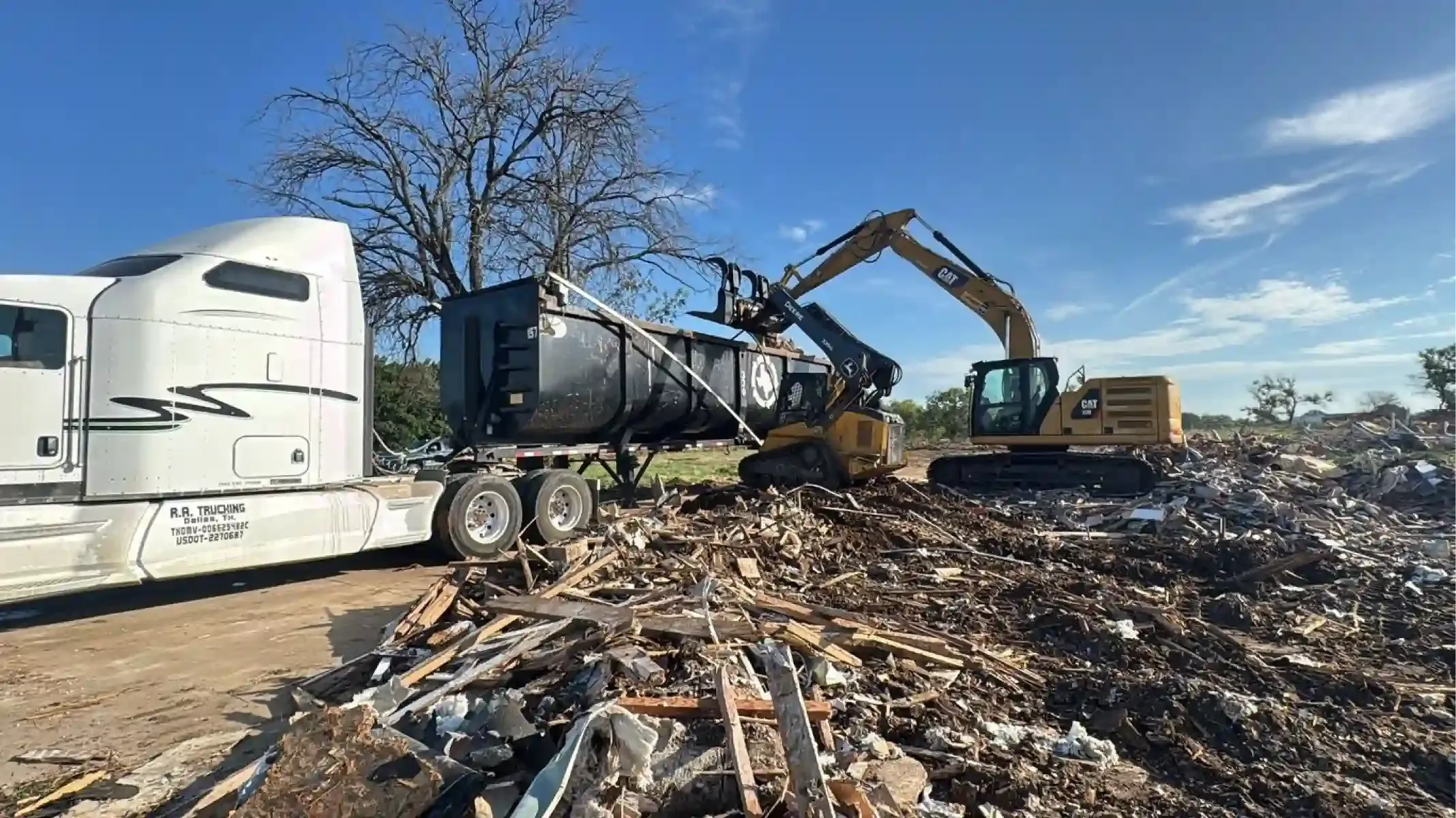 Truck, excavator, and bulldozer in a debris-filled lot under a blue sky.
