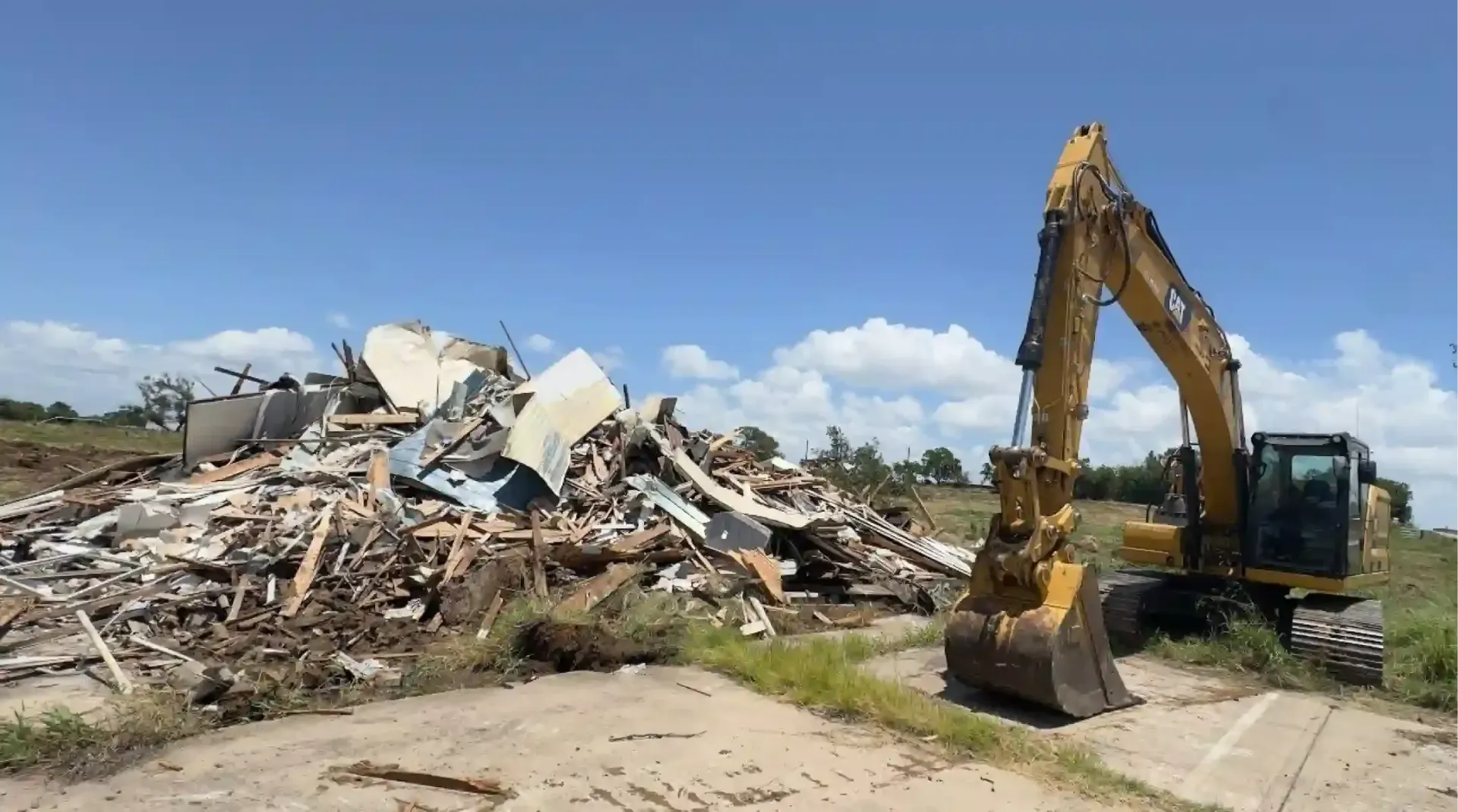 Excavator clearing a large rubble pile under a blue sky at a demolition site