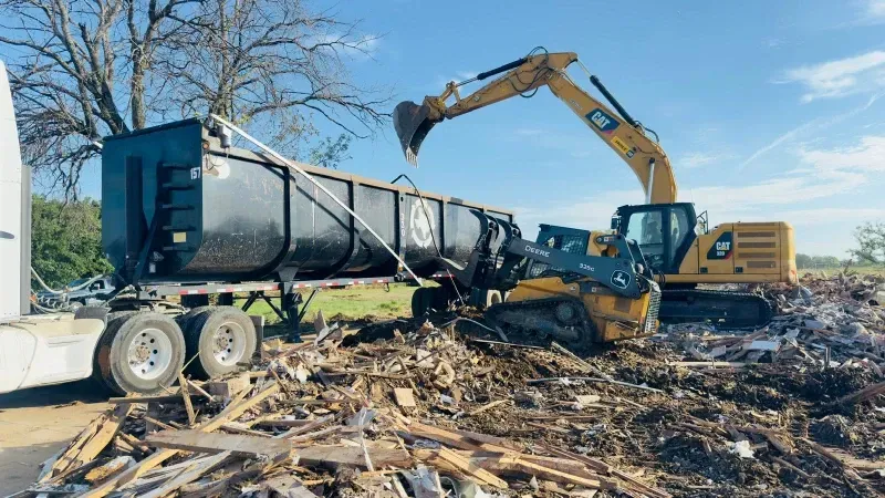Yellow excavator loading debris into a trailer in a demolition site.
