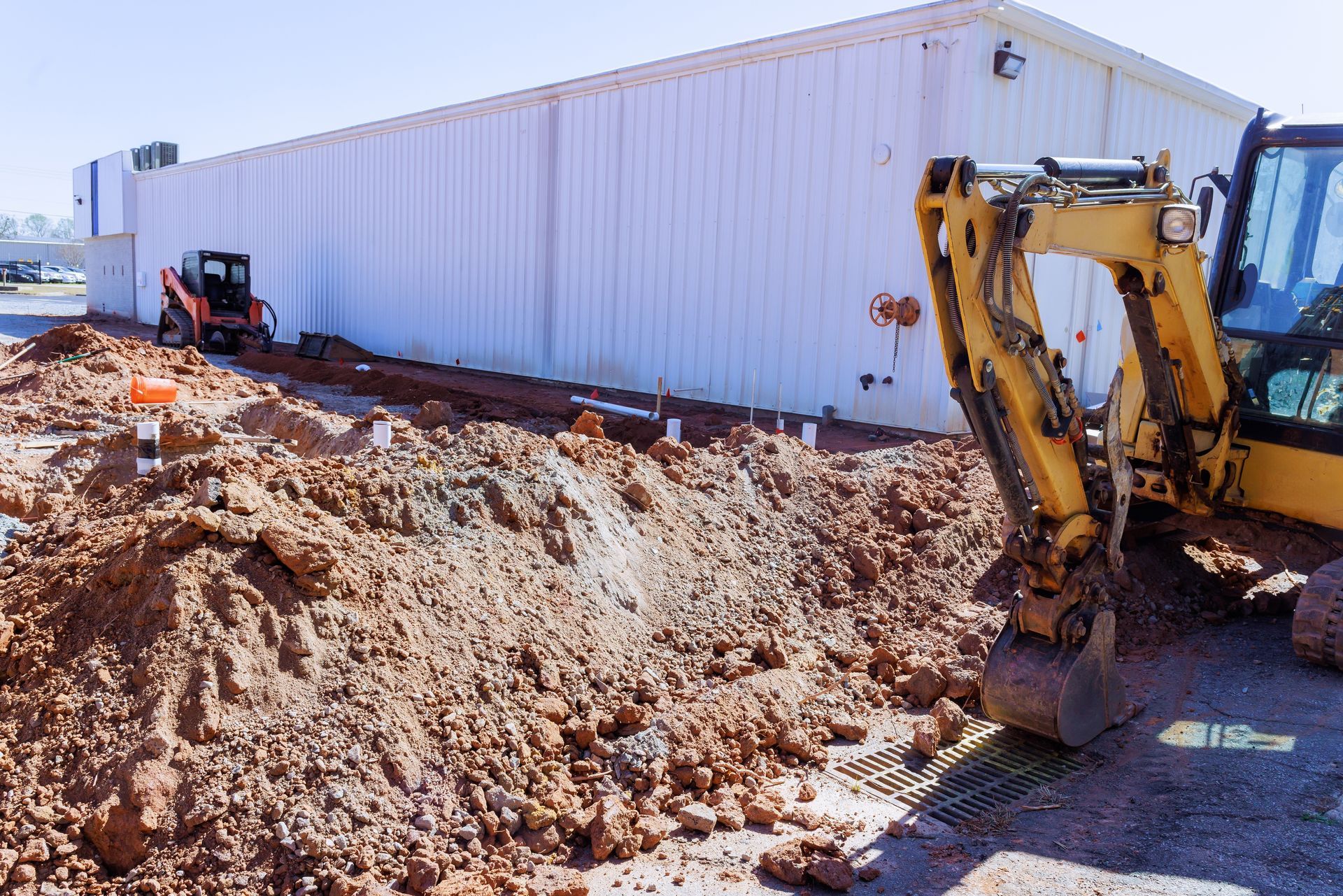 Yellow backhoe digging beside a white industrial building at a construction site