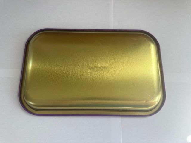 Gold-colored rectangular metal tray with a purple border, on a white surface.