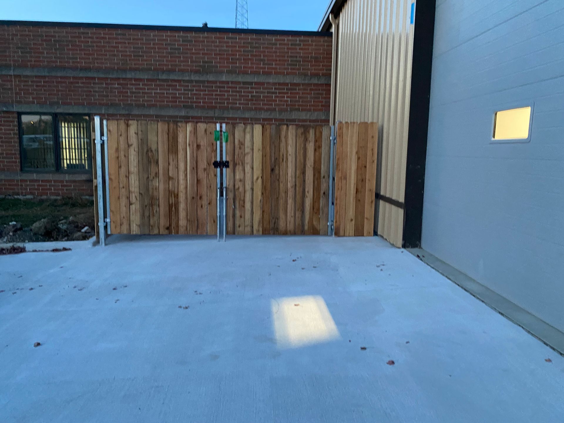 A wooden fence is surrounding a concrete driveway in front of a brick building.