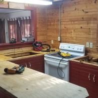 A kitchen under renovation with wooden walls, red cabinets, a white stove, and unfinished wooden countertops.