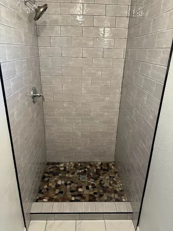 A shower with a tiled wall and a stone floor.